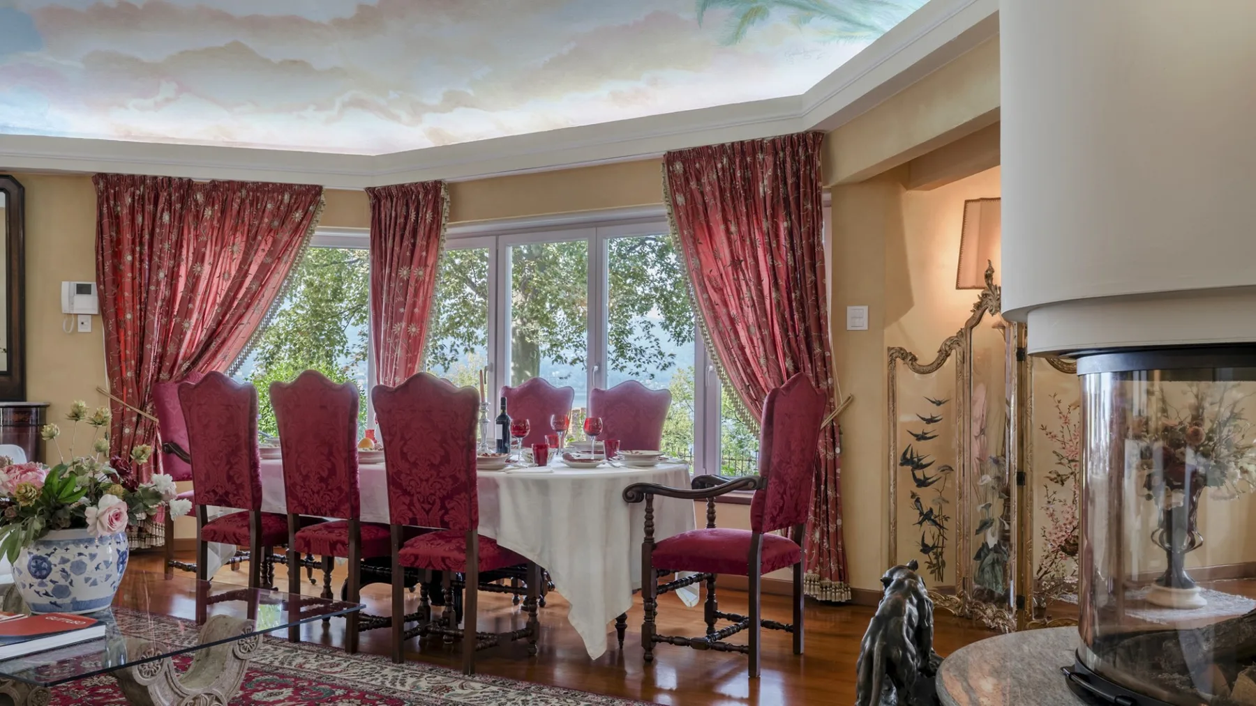 A dining area with red upholstered seating beside large windows.
