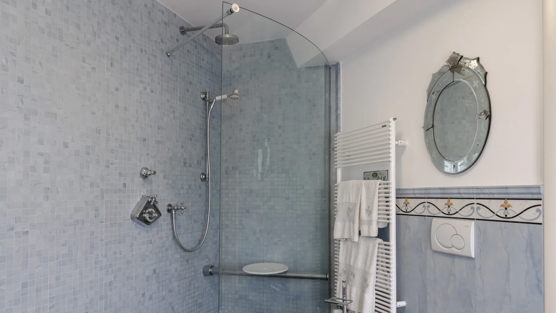 A tiled bathroom with a glass shower and a towel warmer.