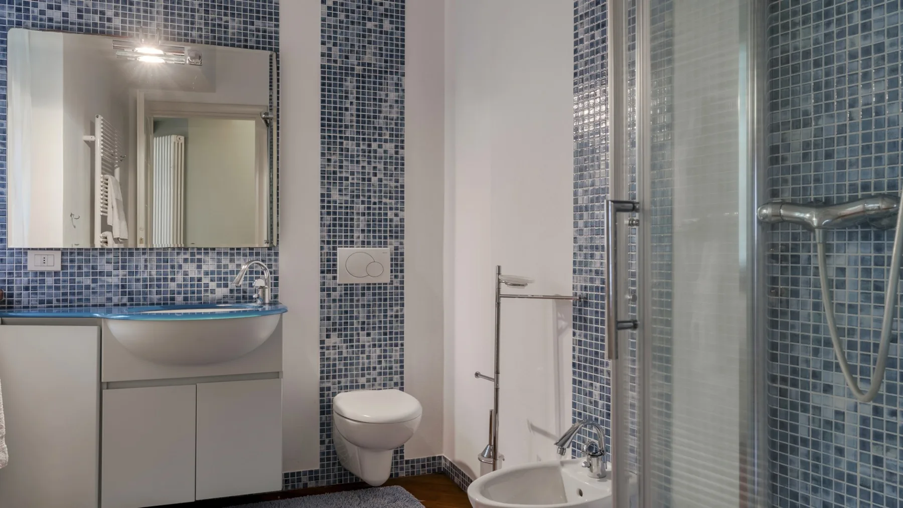 A tiled bathroom with a wall-mounted sink and glass shower.