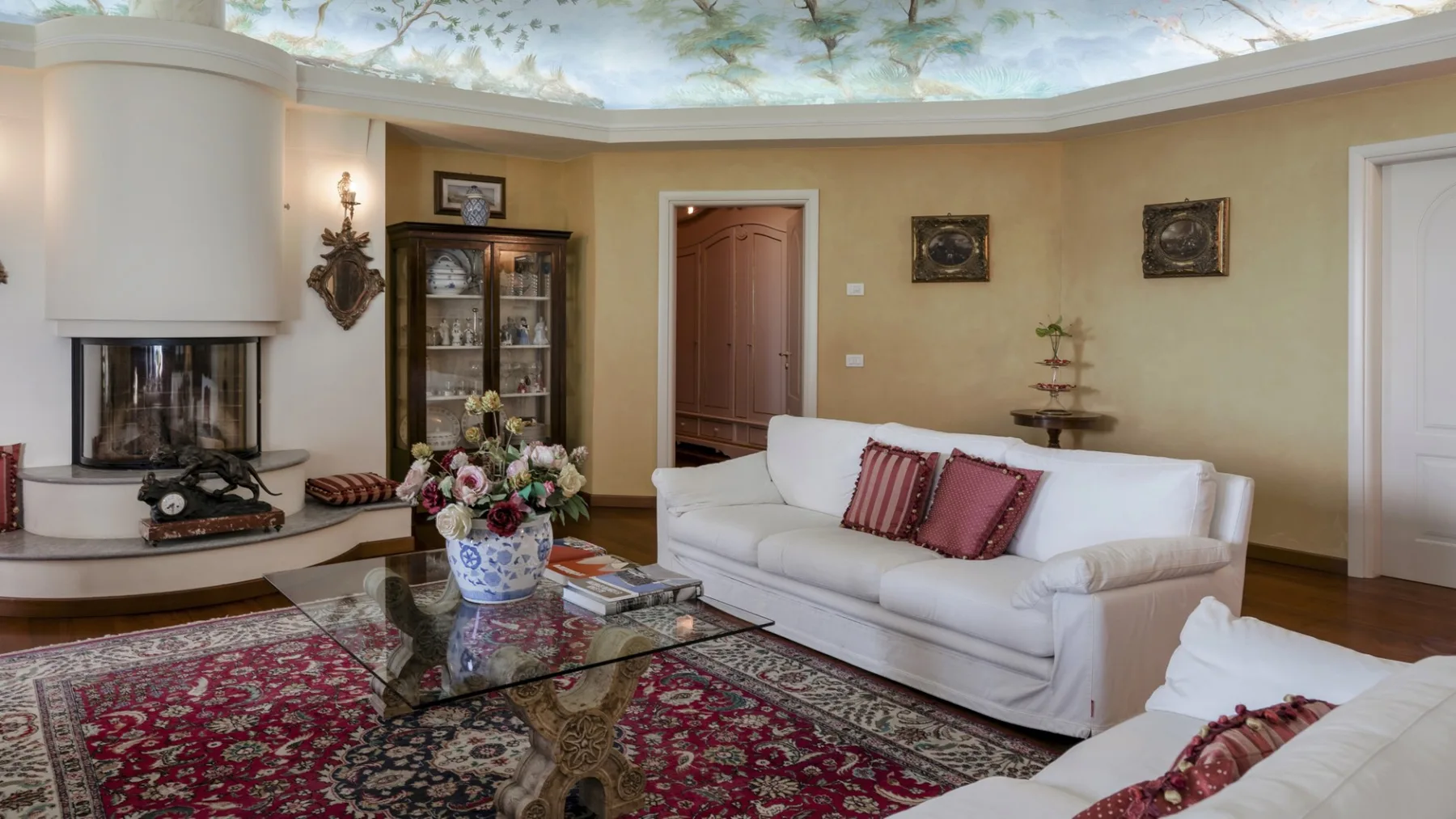 A living room with white seating, a glass coffee table, and a patterned rug.