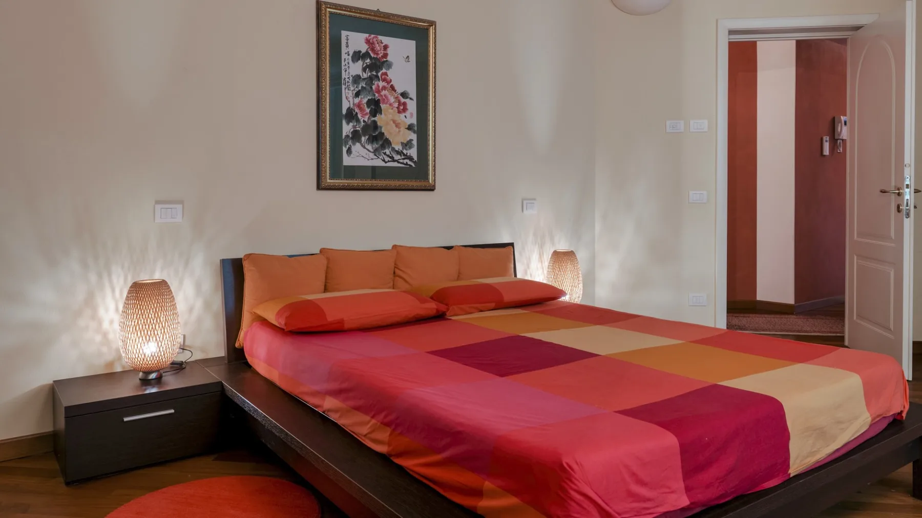 A bedroom with a large bed dressed in a red and orange patchwork bedspread.