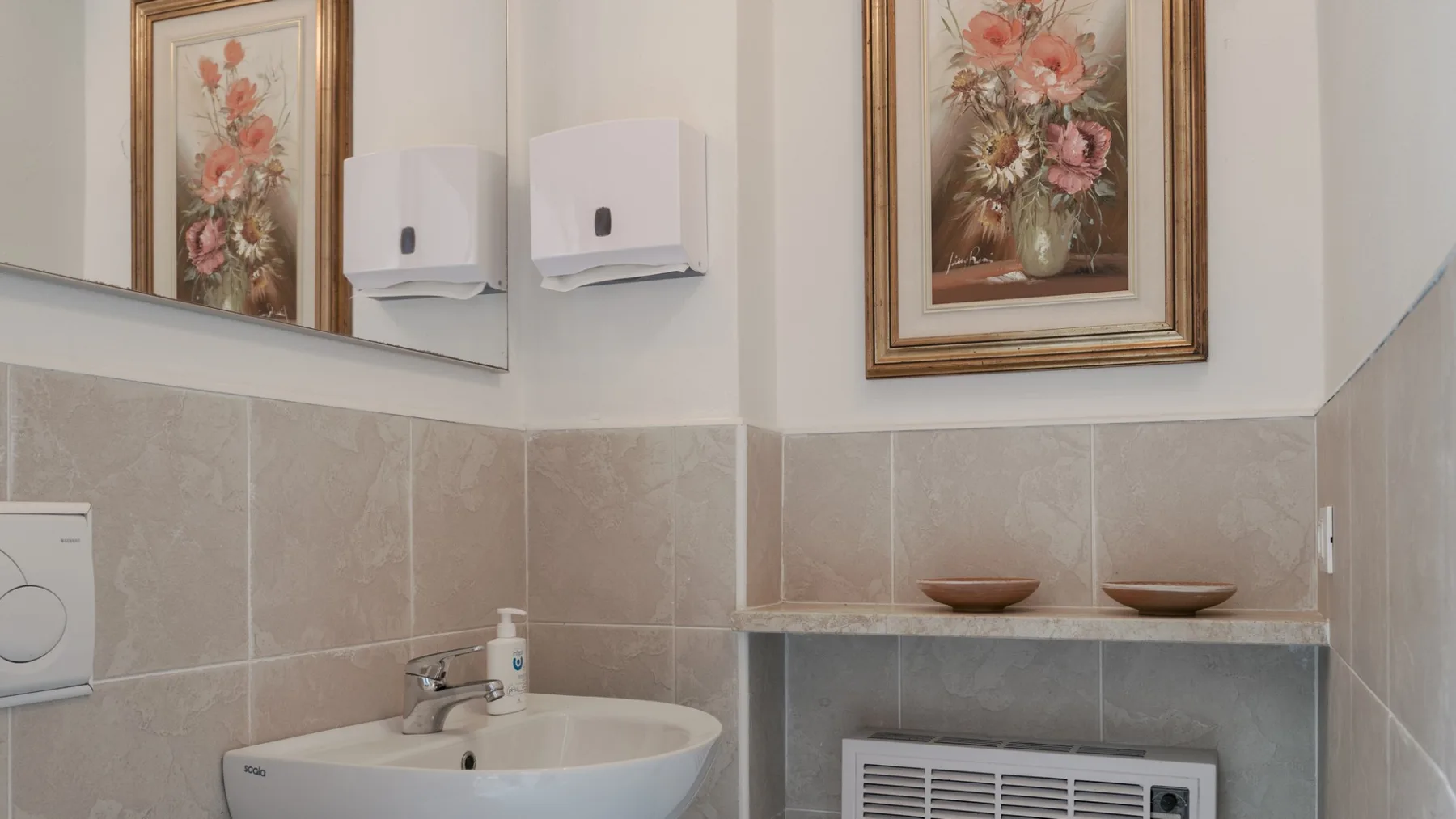 A tiled bathroom with a wall-mounted sink and framed floral prints.