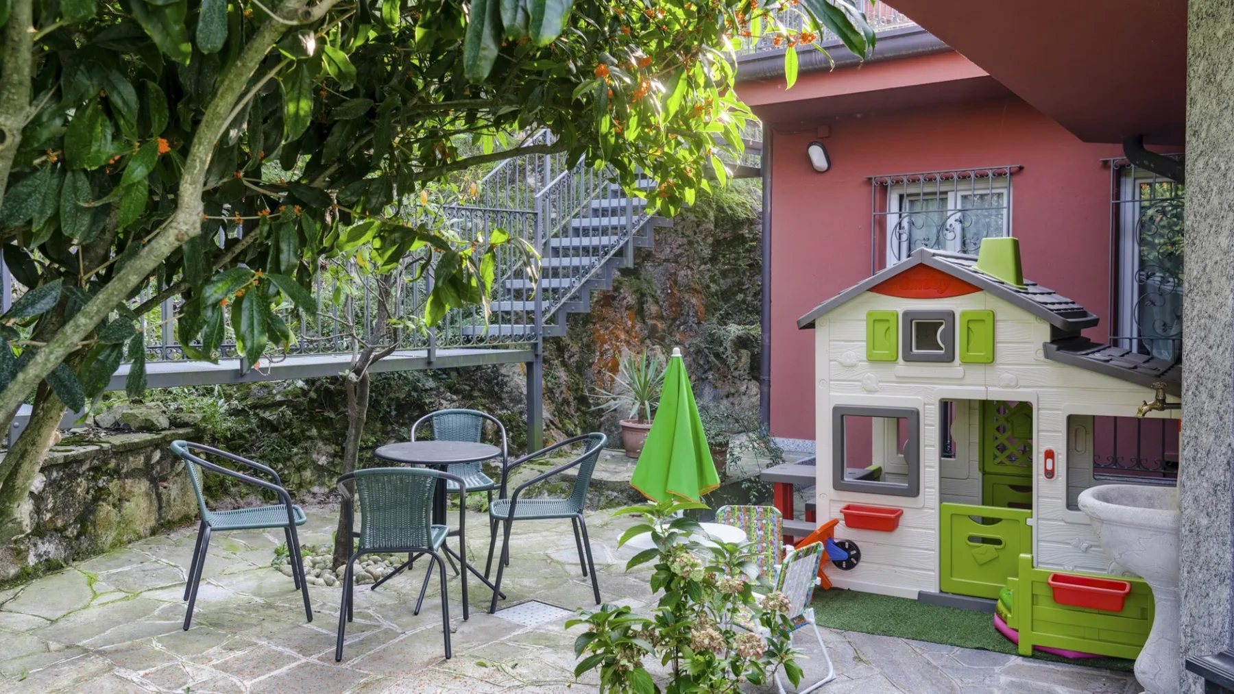 An outdoor patio with seating and a small playhouse beside a pink building.
