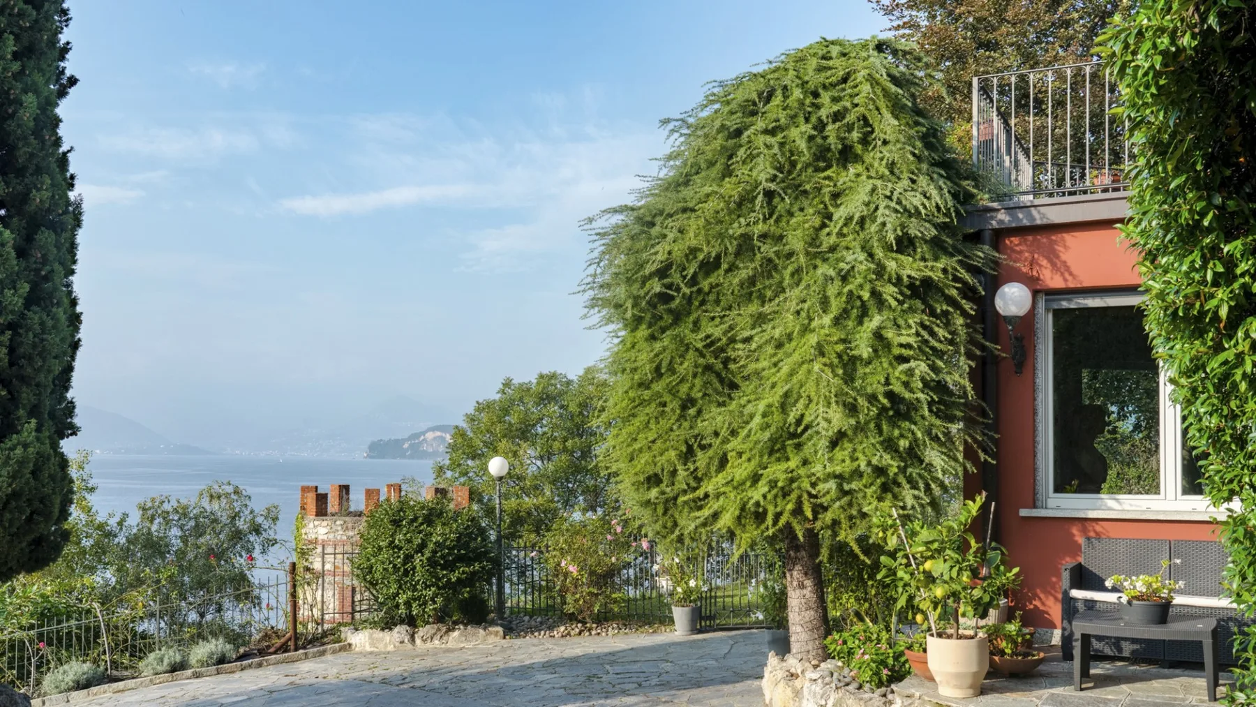 A leafy patio beside a red building overlooks the water.