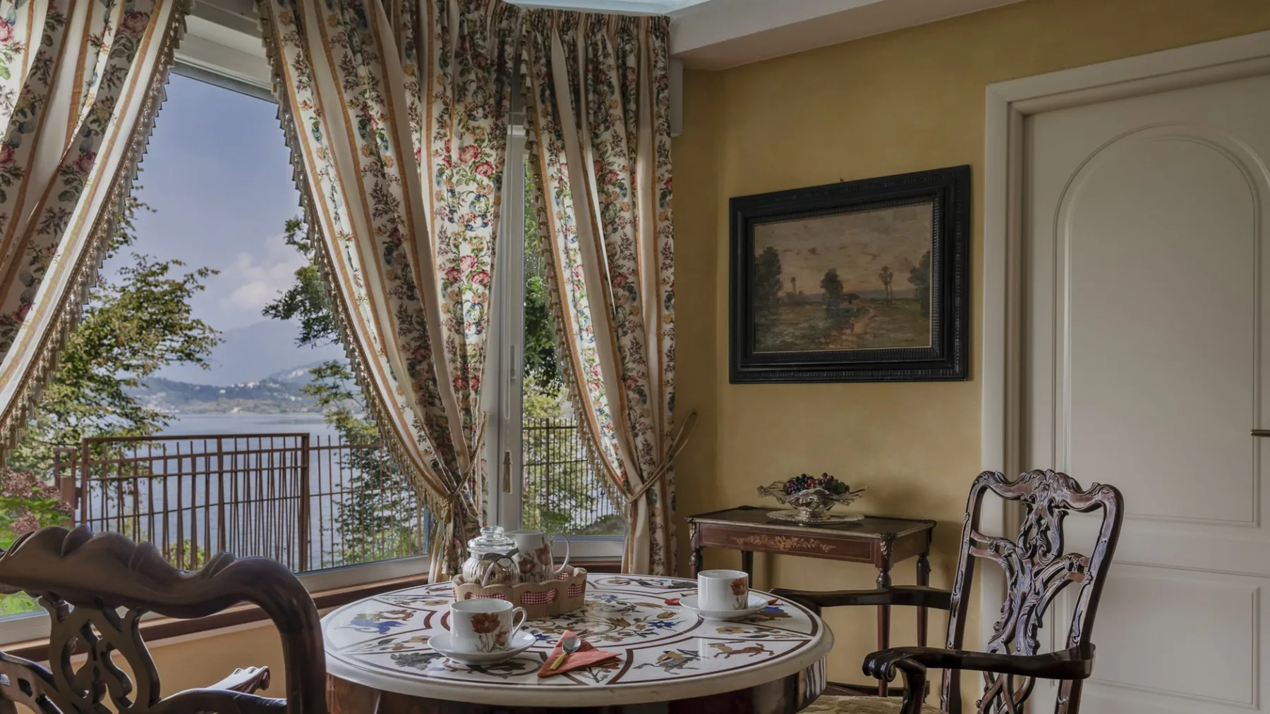 A sitting area with a round table set beside tall windows overlooking a lake.