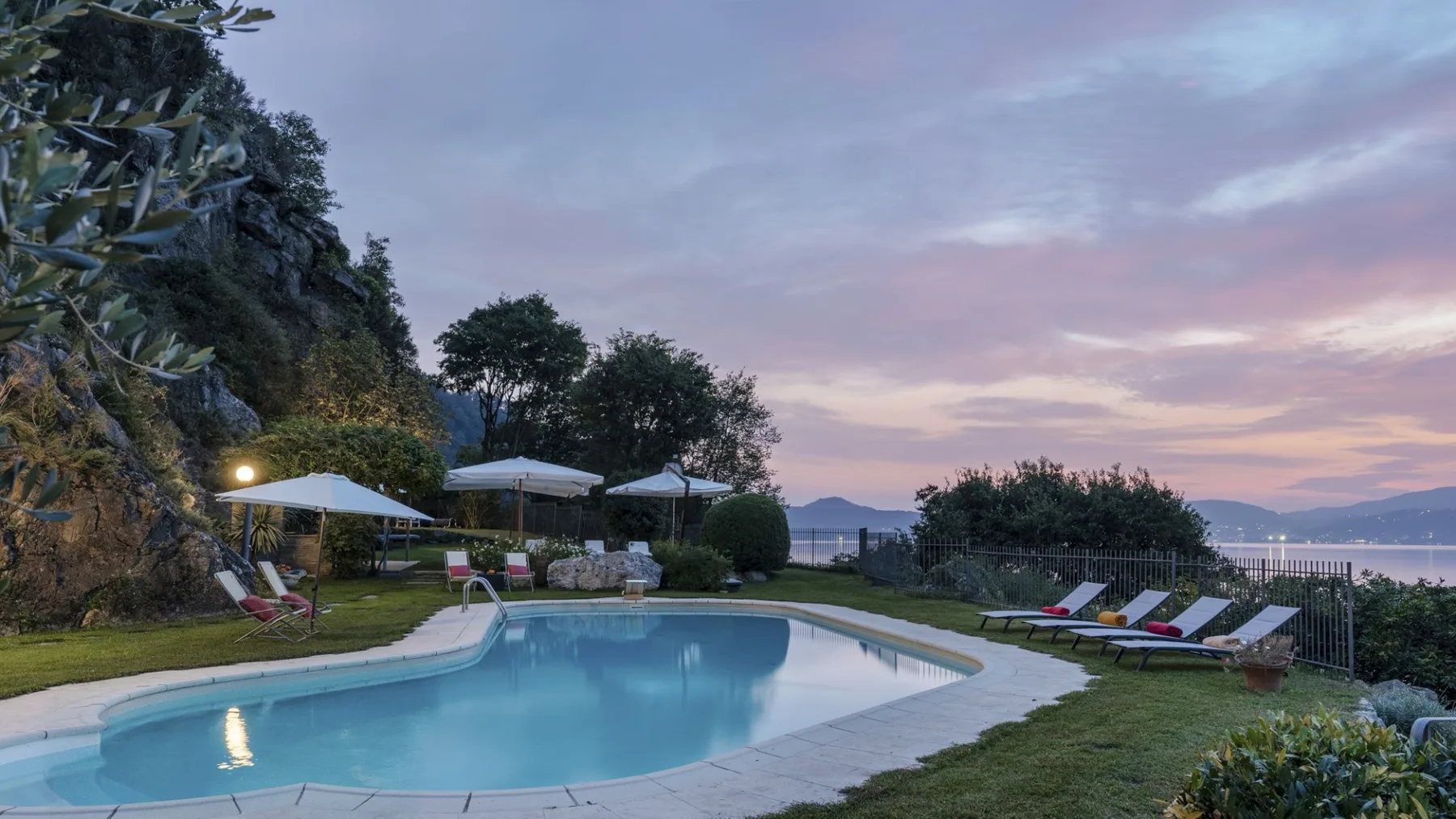 An outdoor swimming pool beside a grassy garden at dusk.