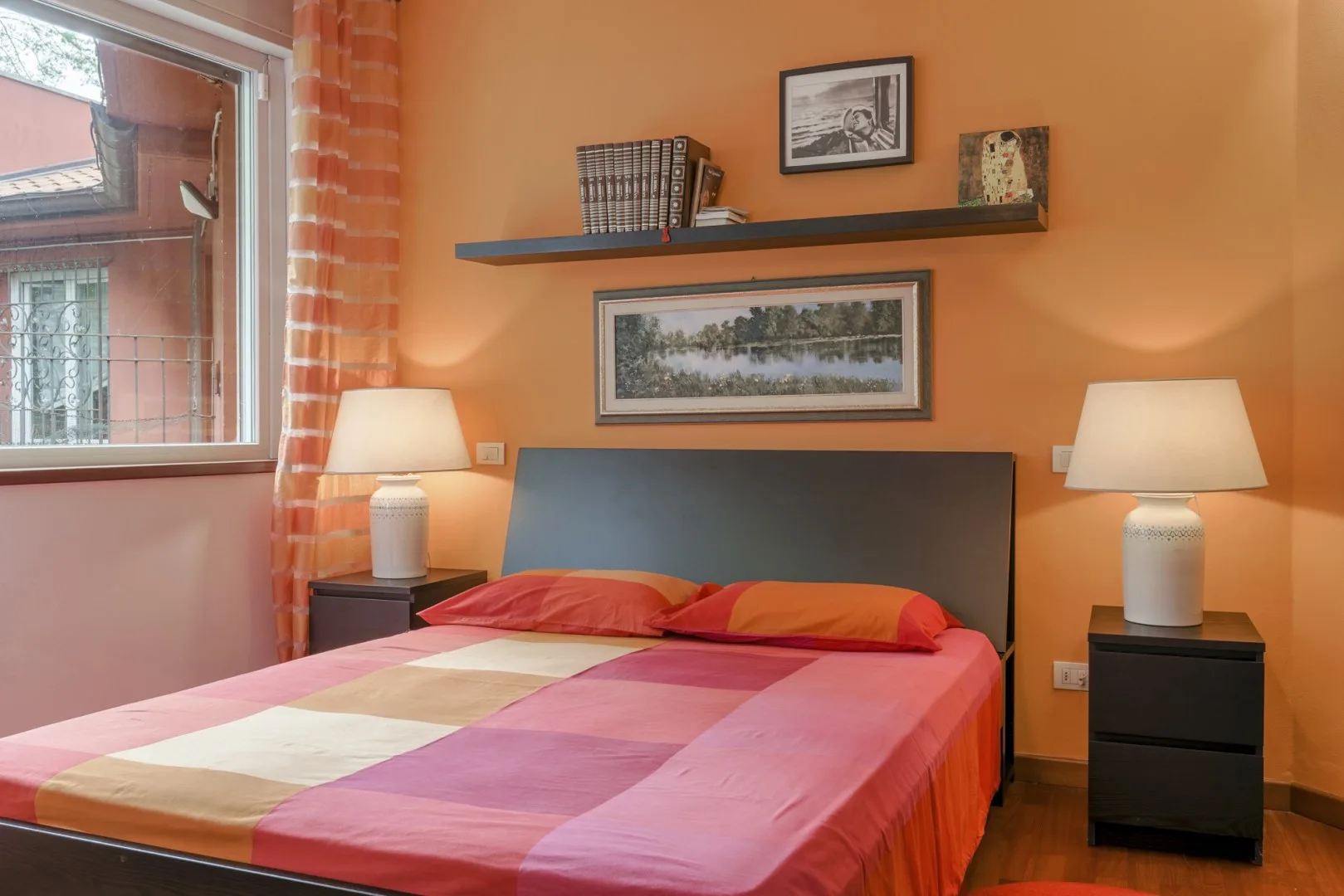 A bedroom with a bed dressed in colorful patchwork bedding and matching bedside lamps.