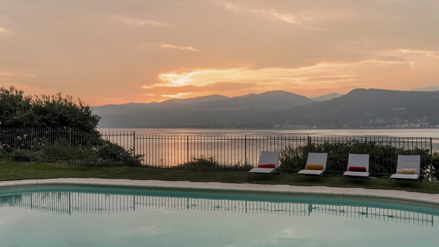 An outdoor swimming pool overlooks a lake and distant mountains at sunset.