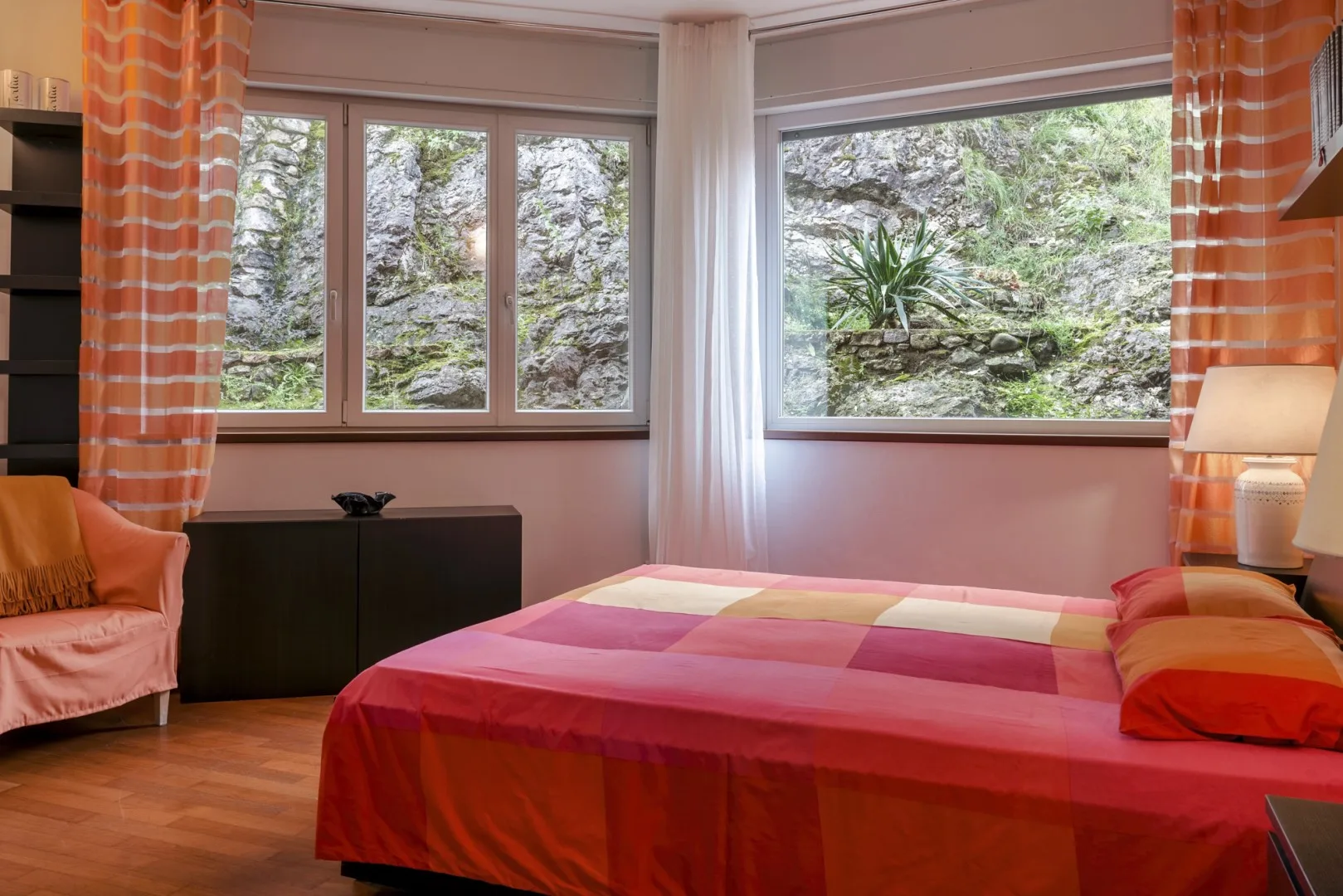 A bedroom with a colorful bedspread and large windows overlooking greenery.