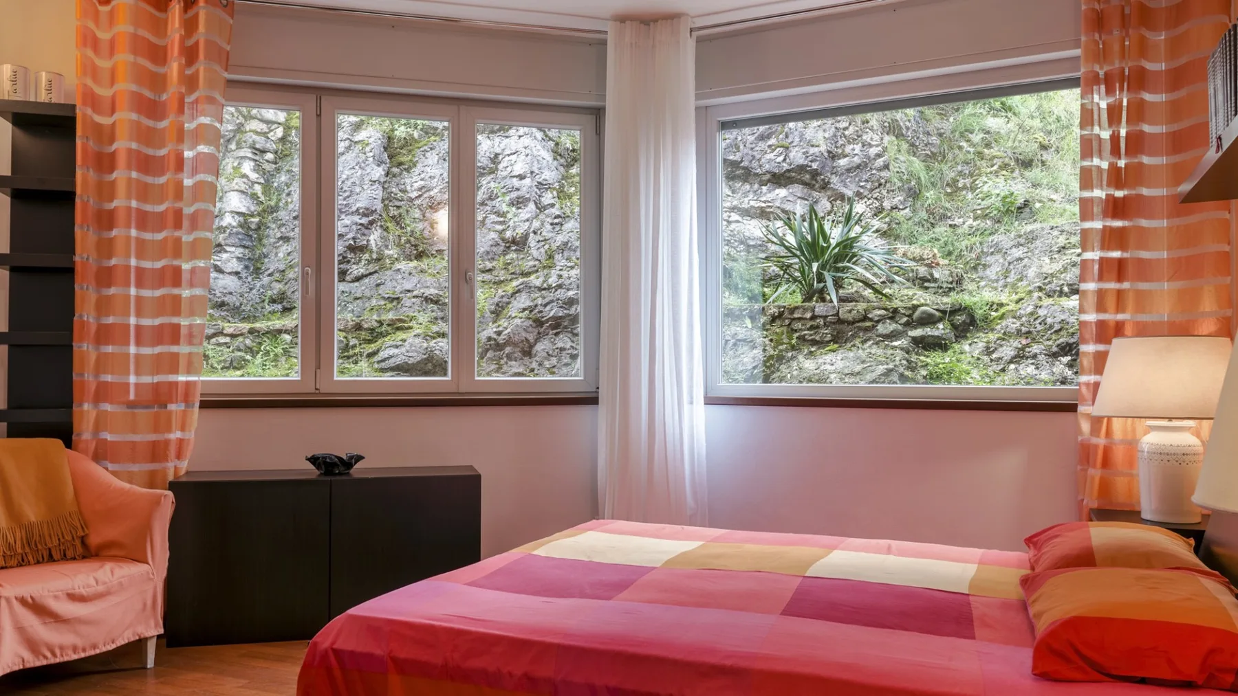 A bedroom with a bed covered in a colorful patchwork quilt beside large windows.