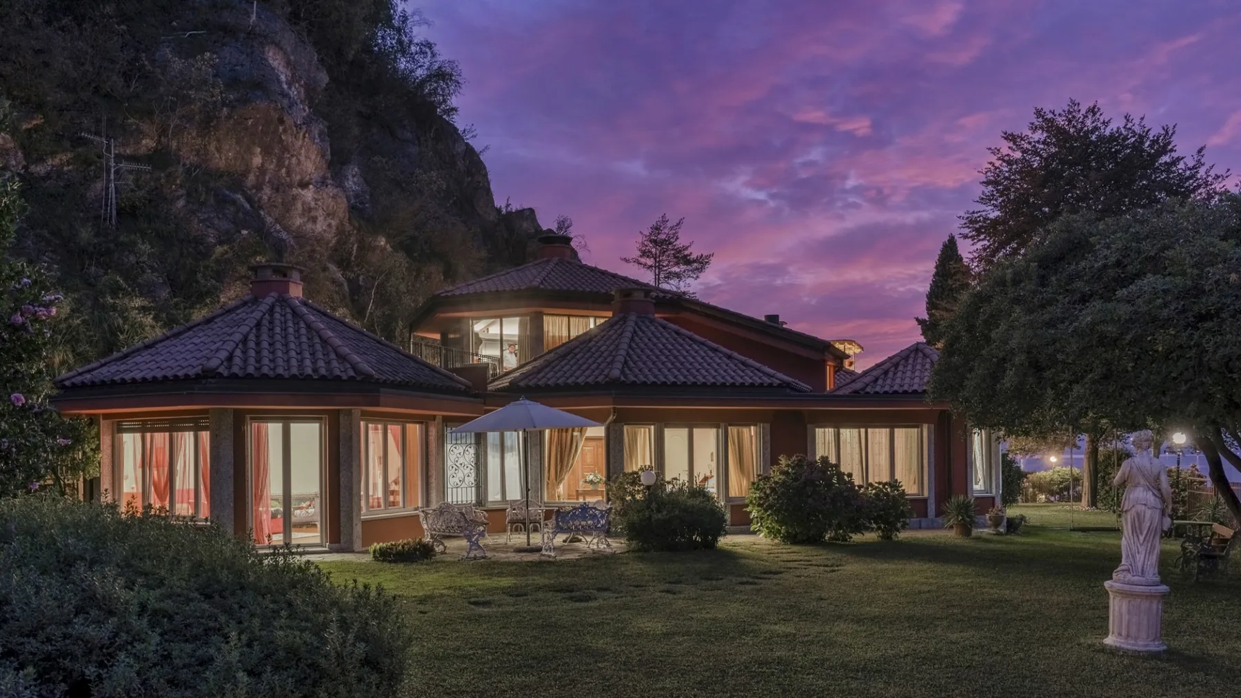 A low house with a broad lawn sits beneath a colorful dusk sky.