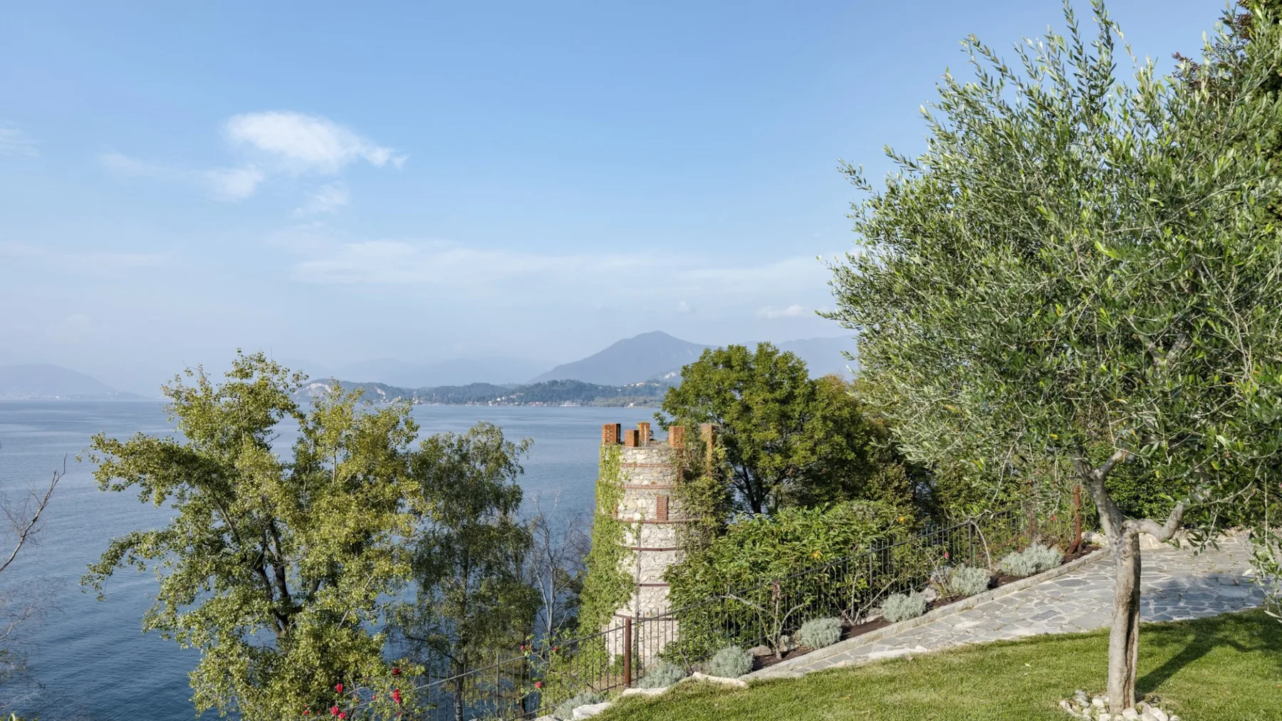 A lakeside scene with trees, a grassy slope, and distant mountains.