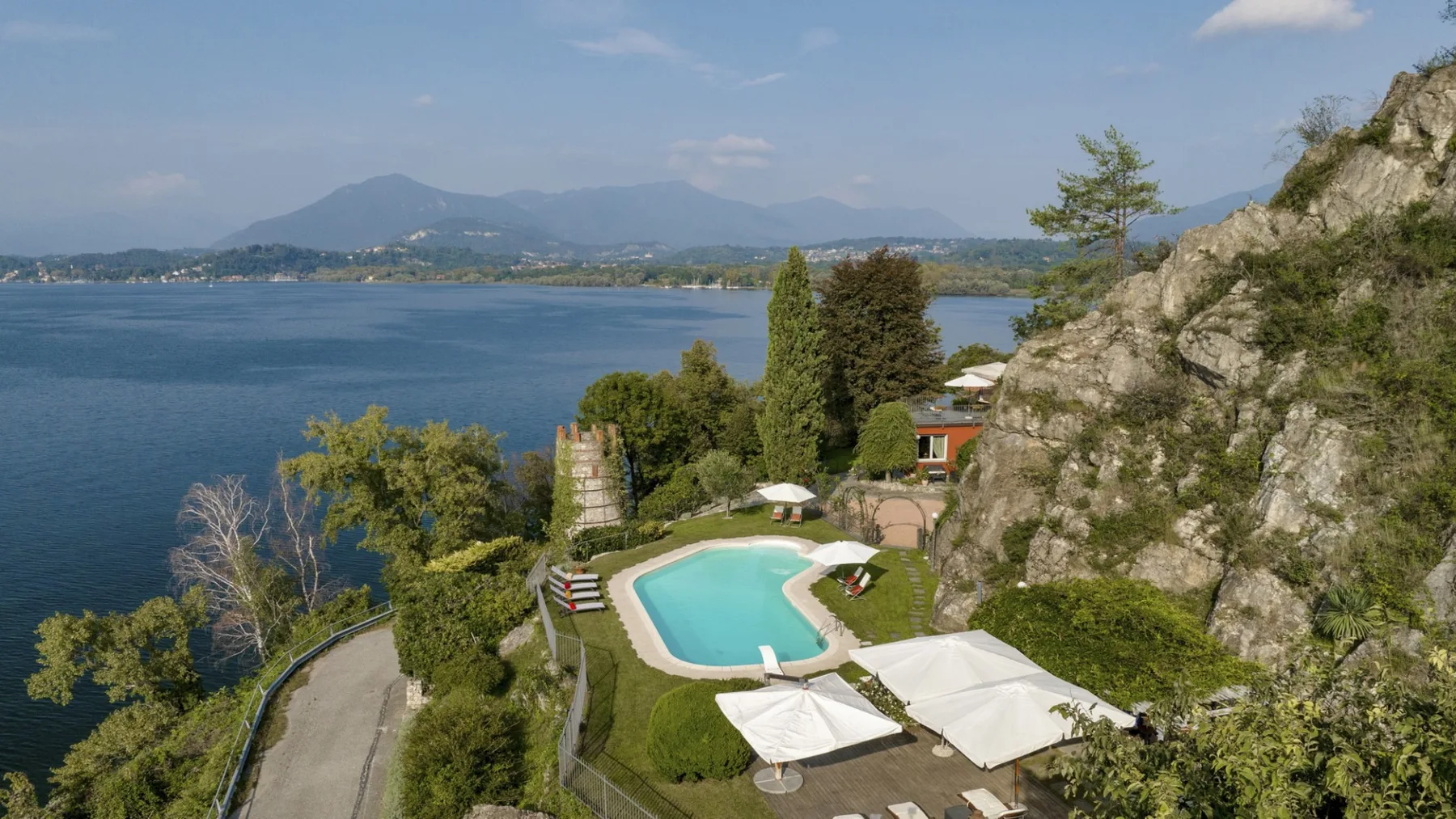 A lakeside outdoor pool sits among landscaped grounds, with mountains across the water.