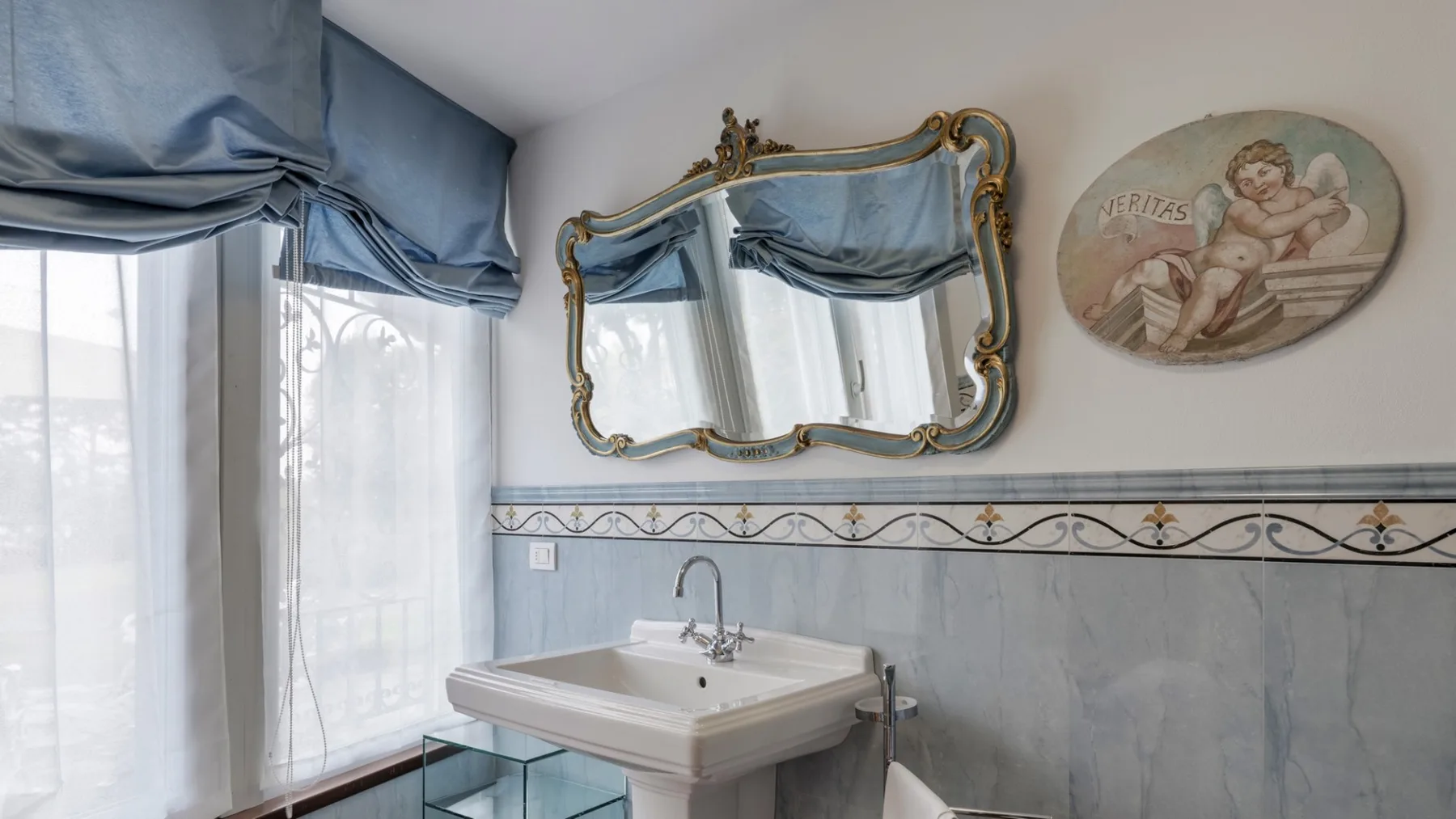 A bathroom with a pedestal sink, tiled walls, and an ornate wall mirror.