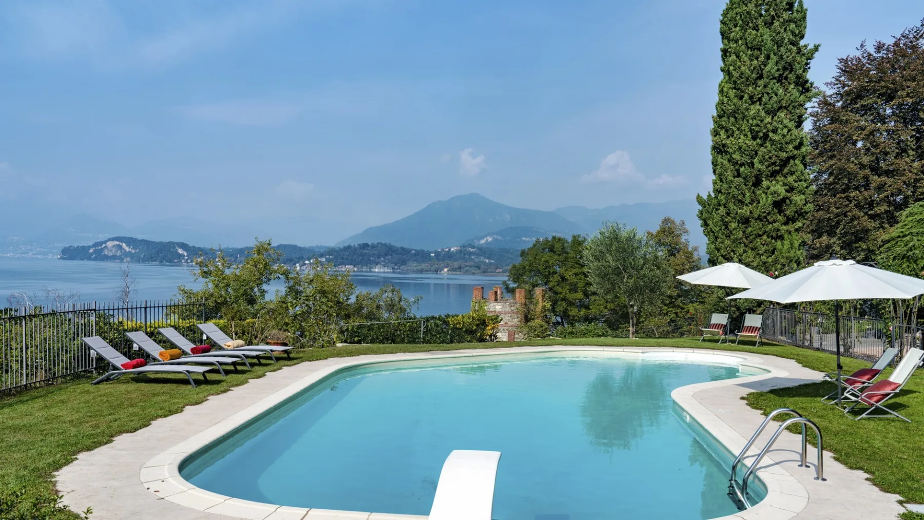 An outdoor swimming pool overlooks a lake and distant mountains.