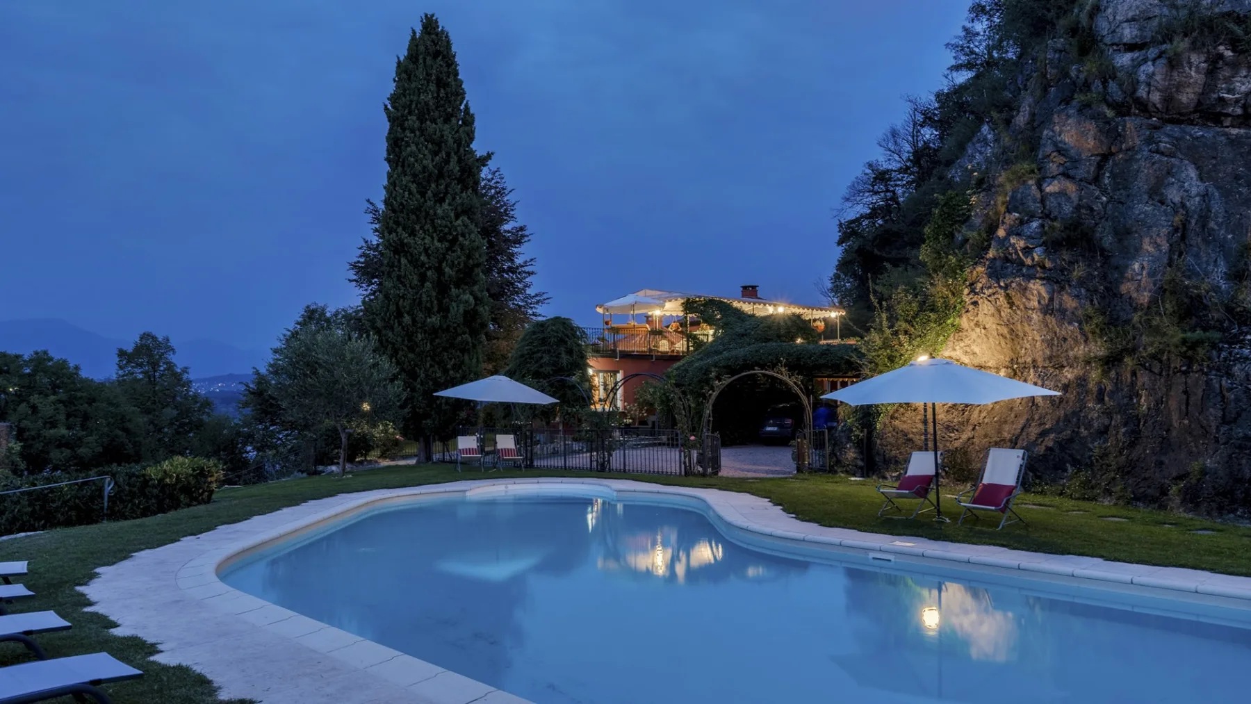 An outdoor swimming pool at dusk, with lounge seating and a rocky hillside.