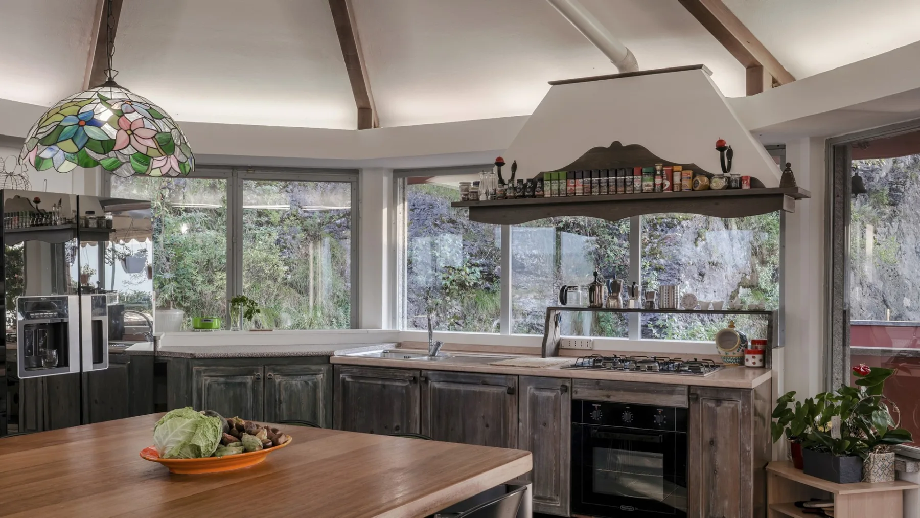 A kitchen with a wide wooden island and large windows overlooking greenery.