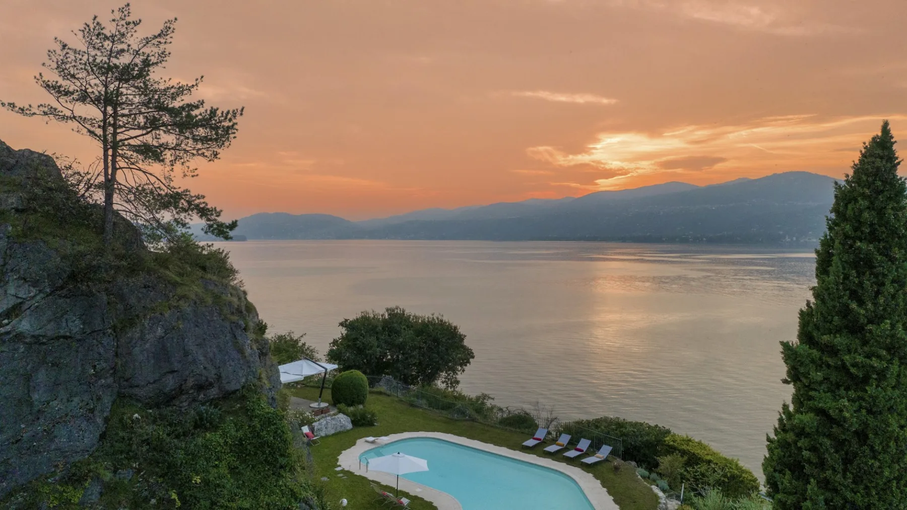 A lakeside pool and garden overlook calm water beneath a sunset sky.