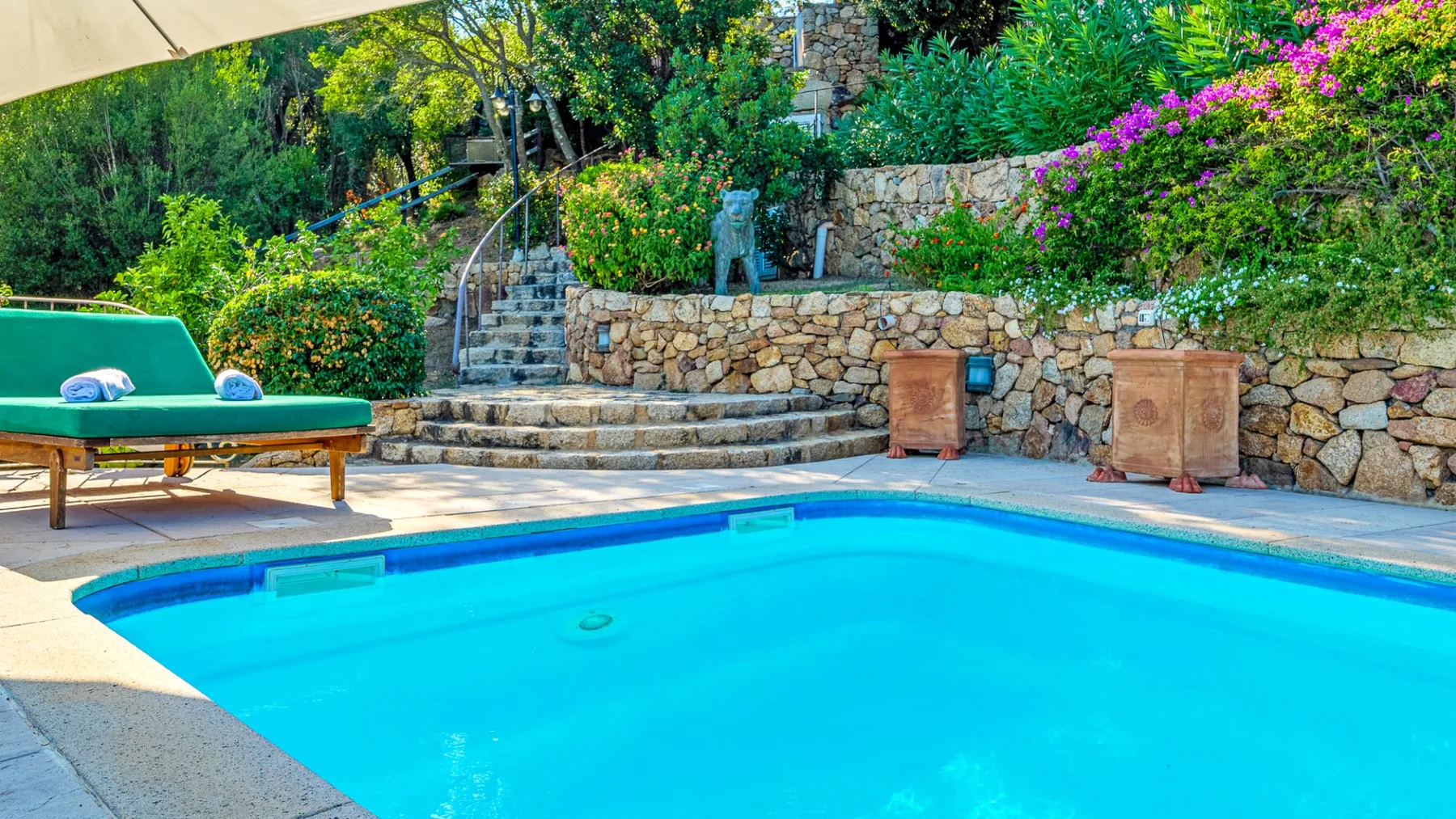Una piscina al aire libre está junto a escalones de piedra y vegetación.