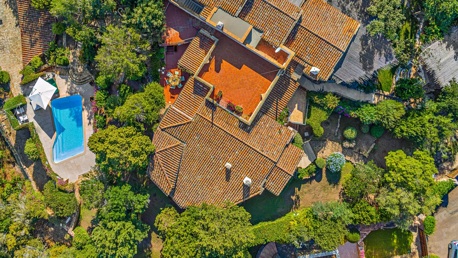 Vista aérea de una casa con tejado de tejas rodeada de árboles, con una piscina cerca.