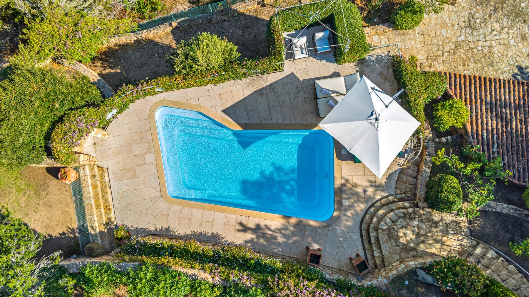 Una piscina está en una zona exterior pavimentada junto a una gran sombrilla.
