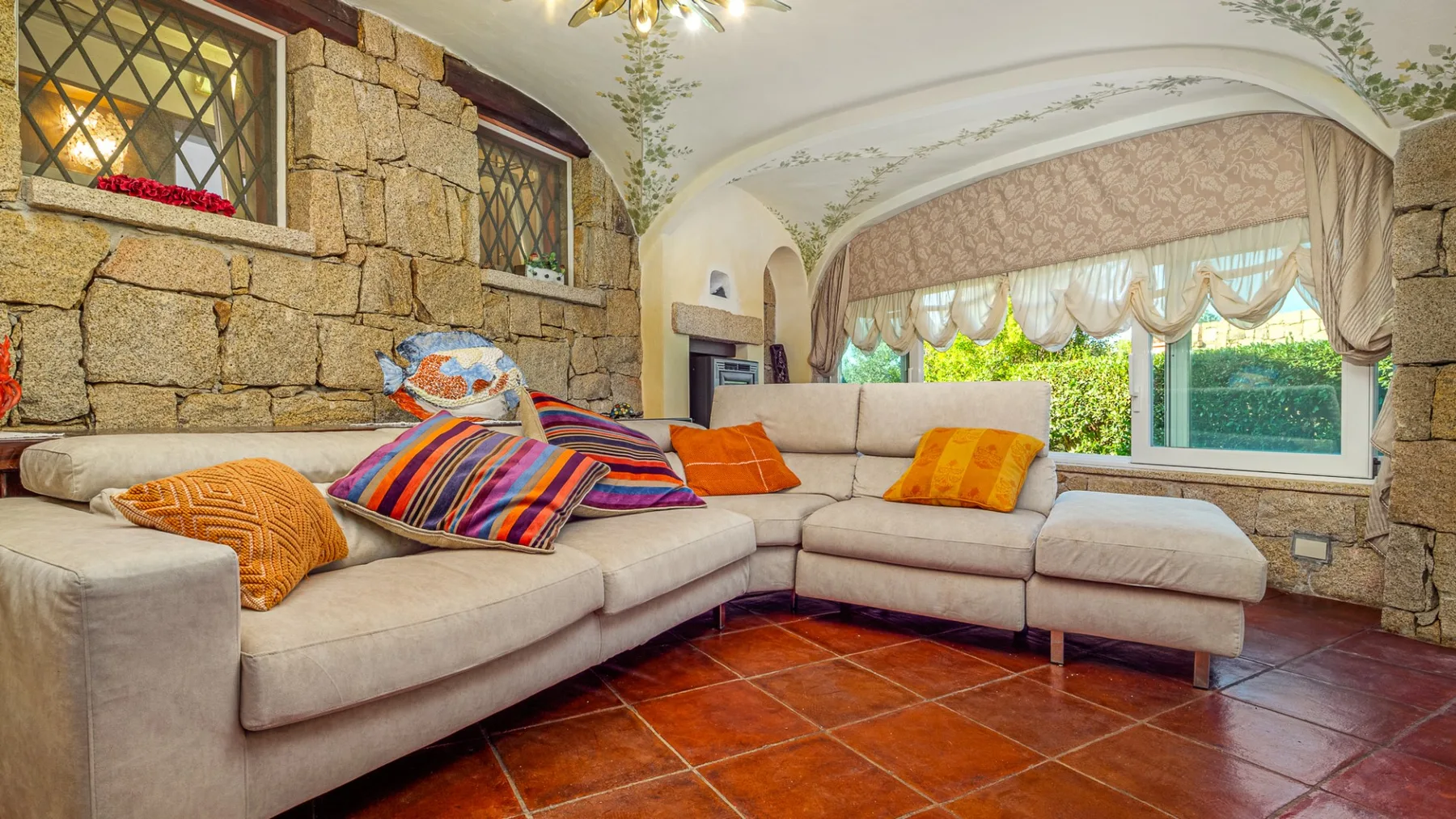 Una sala de estar con asientos seccionales, cojines coloridos y ventanas grandes.