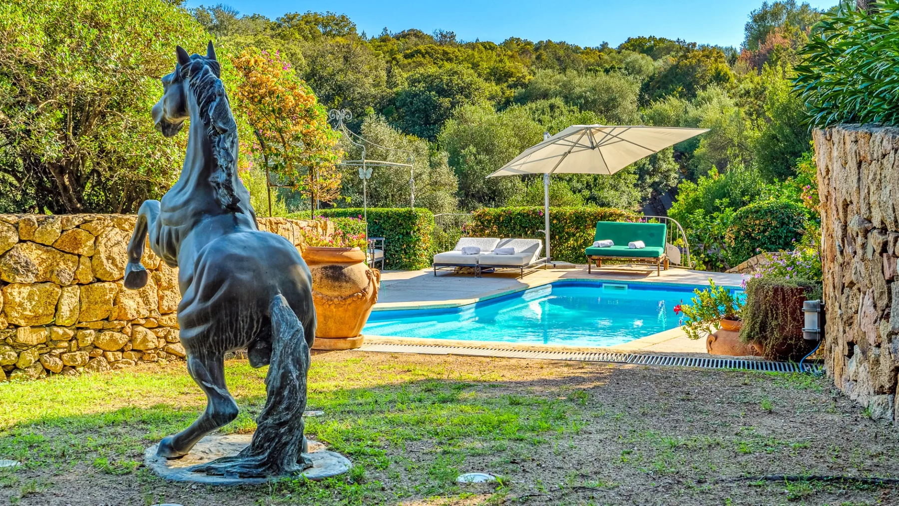 Una piscina está rodeada de vegetación, con una estatua de caballo encabritado en primer plano.