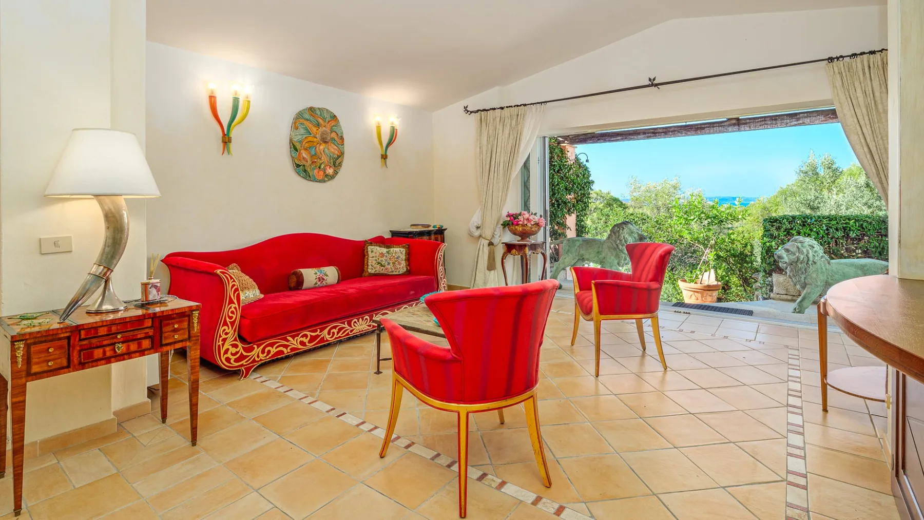 Una sala luminosa con asientos rojos y puertas abiertas hacia un jardín.