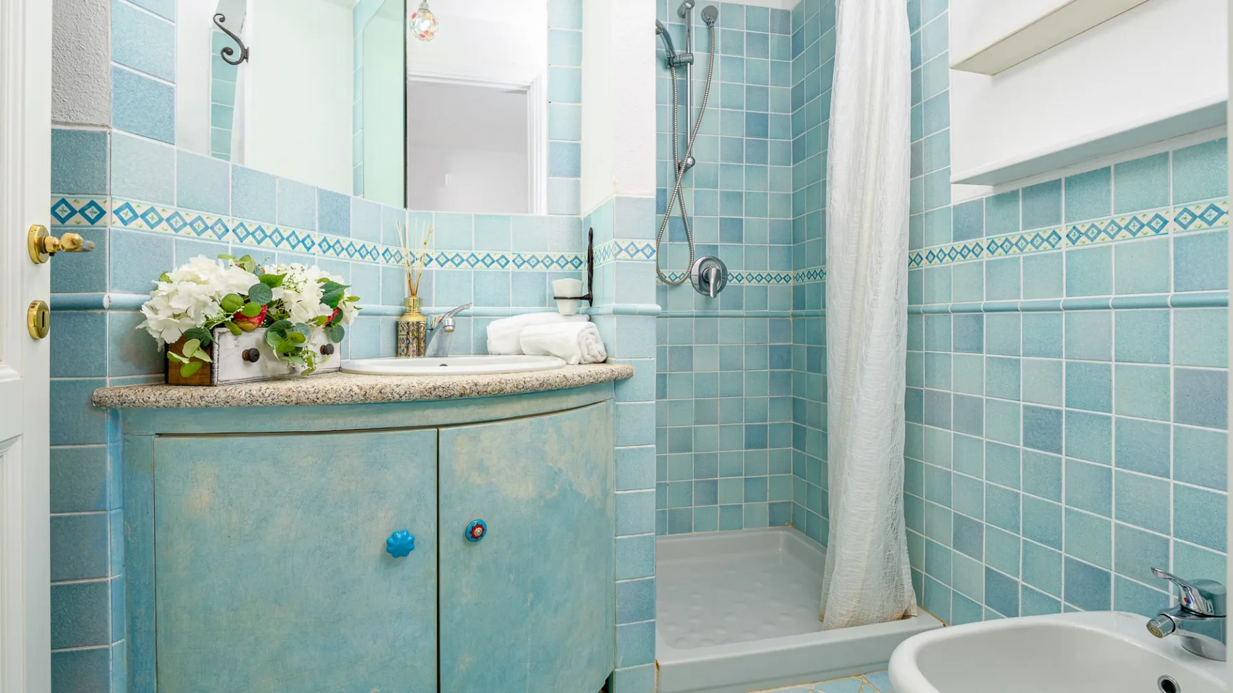Un baño alicatado con tocador, espejo y ducha.