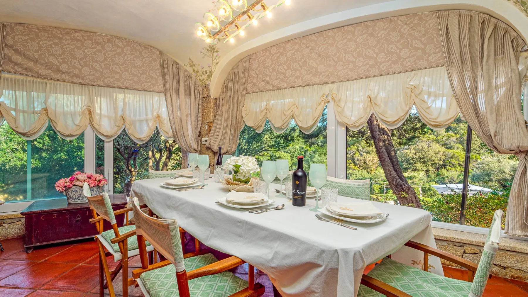 Comedor con una mesa preparada para comer junto a grandes ventanas con cortinas.