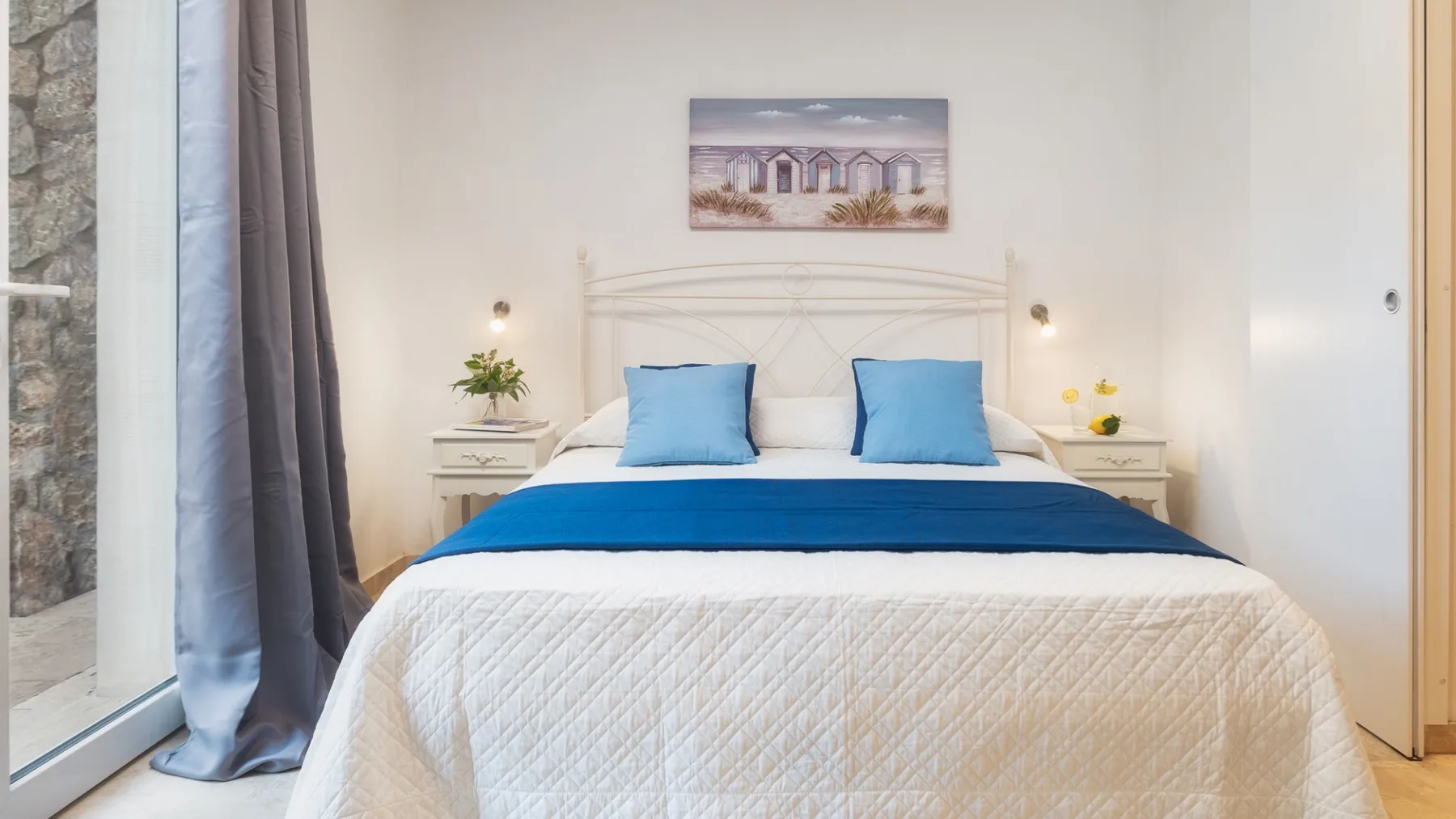 Un dormitorio con una cama blanca, almohadas azules y mesitas de noche a juego.