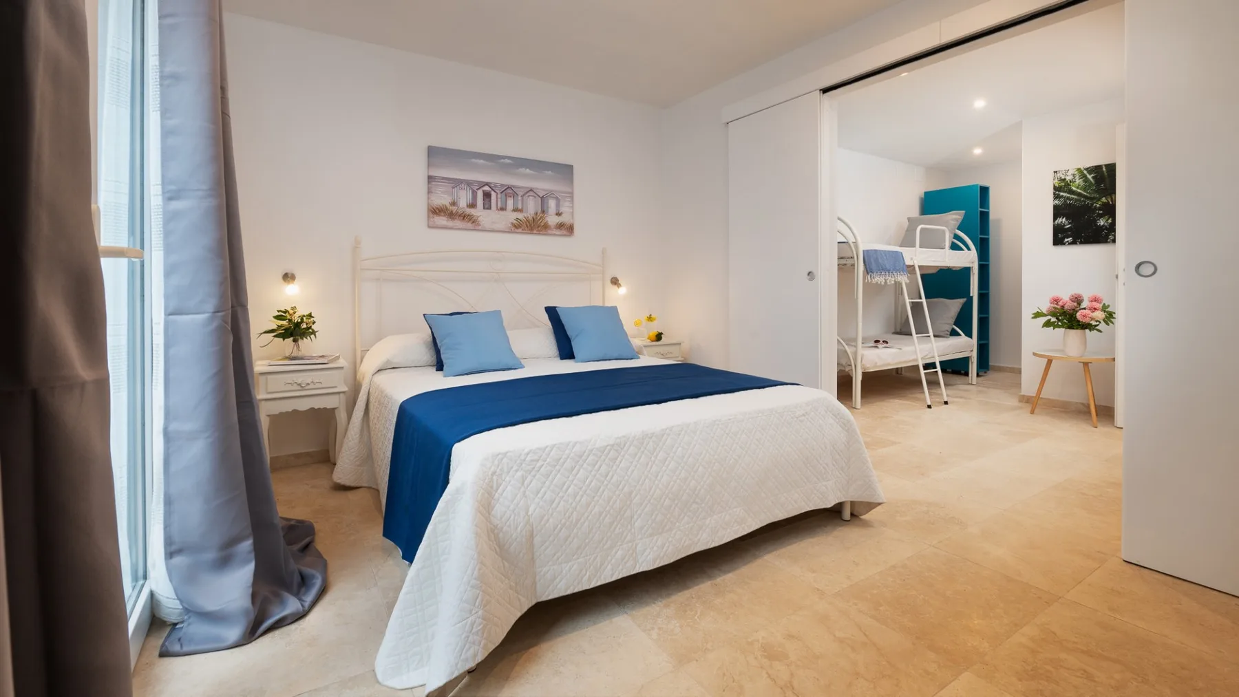 Un dormitorio luminoso con una cama azul y blanca y una zona contigua con literas.