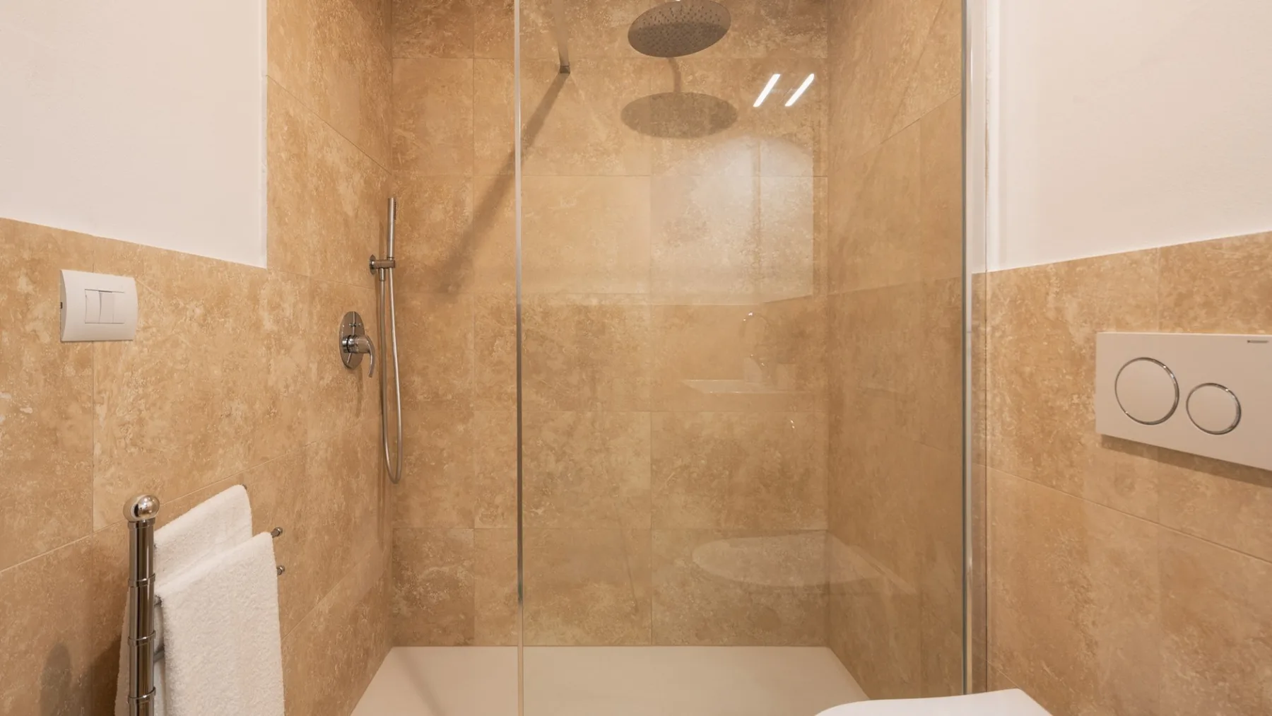 Una ducha de baño con paredes color beige y una mampara de vidrio.
