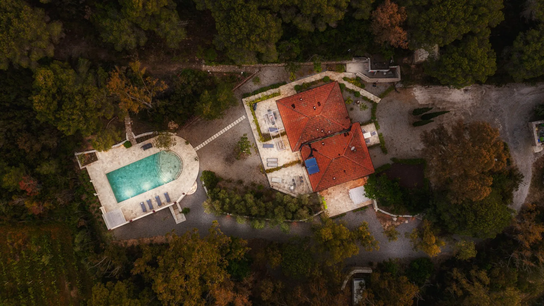 Vista aérea de un edificio con techo rojo junto a una piscina, rodeado de árboles.