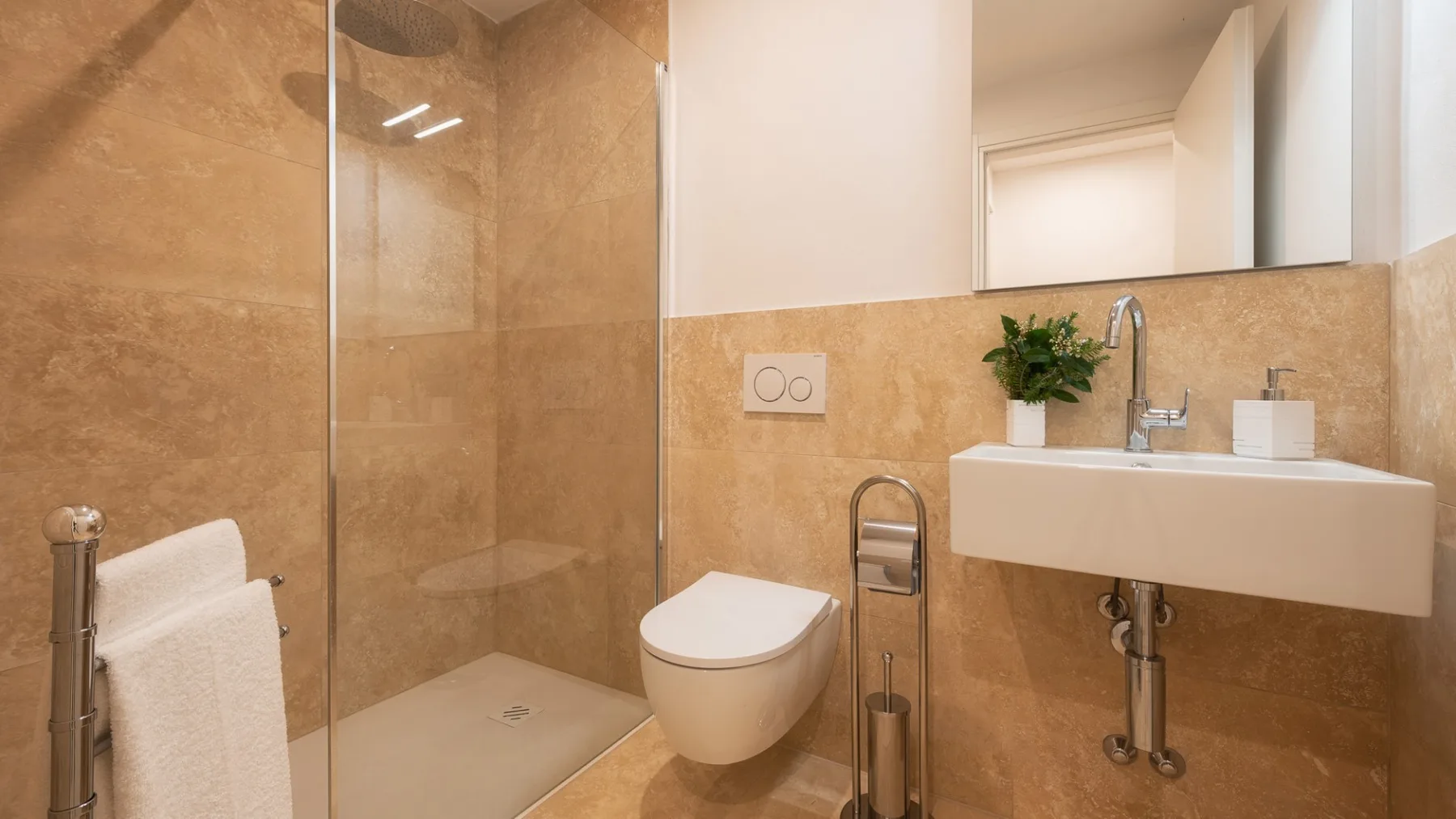 Un baño con ducha de vidrio, inodoro y lavabo suspendido.