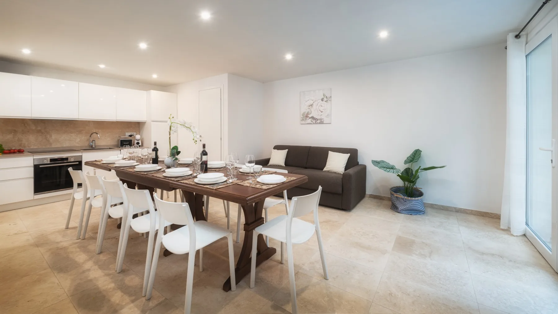 Comedor con la mesa puesta junto a una cocina abierta y un sofá oscuro.