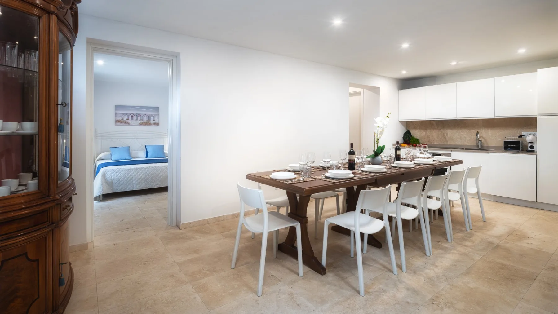 Comedor con una mesa puesta junto a una cocina abierta y la entrada a un dormitorio.