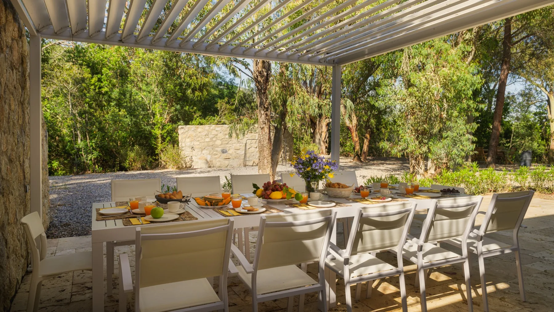 Una zona de comedor exterior sombreada, con una mesa larga bajo una pérgola de listones.