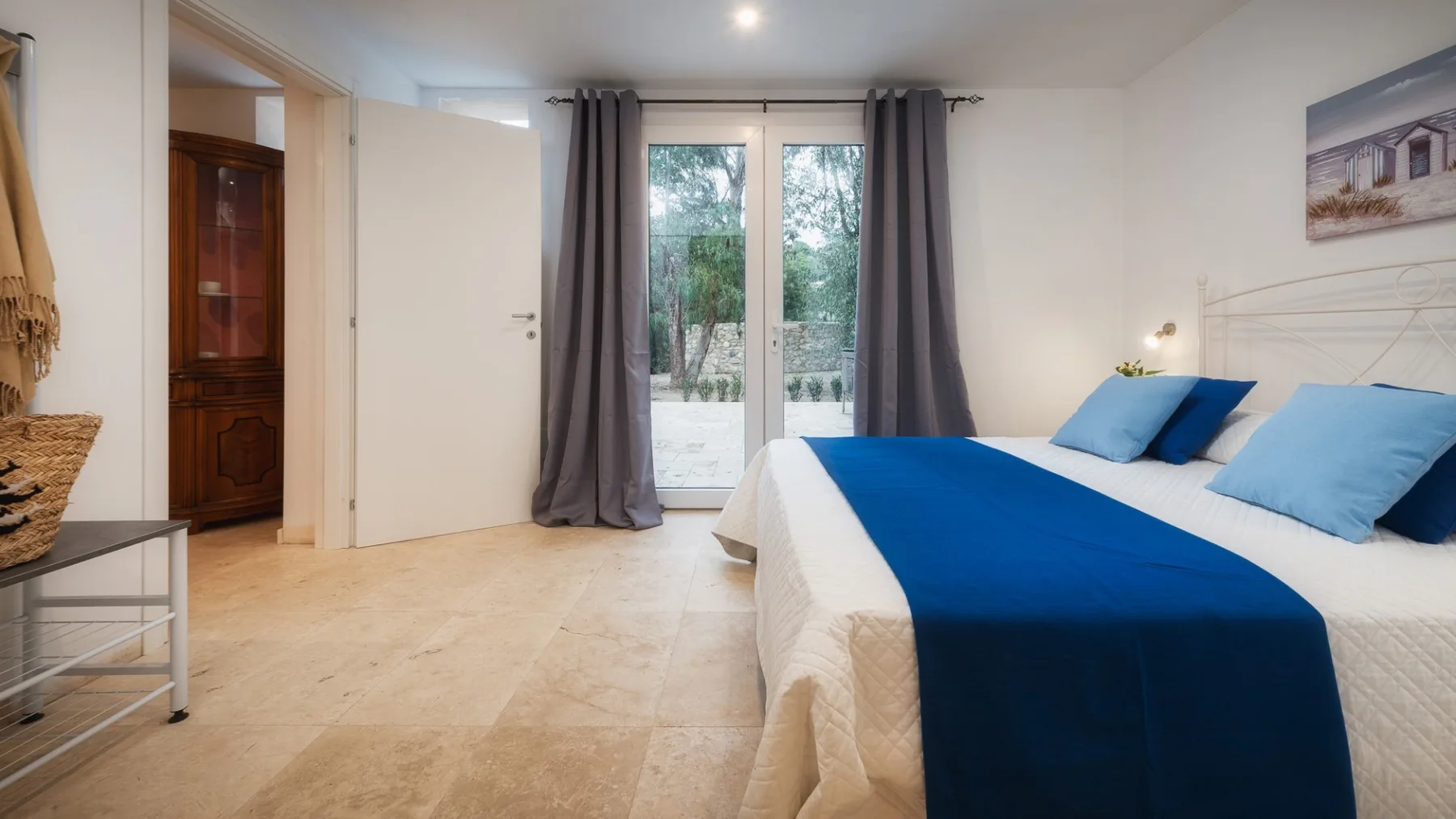Un dormitorio con una cama cubierta por una colcha azul y puertas de vidrio con vistas a la vegetación.