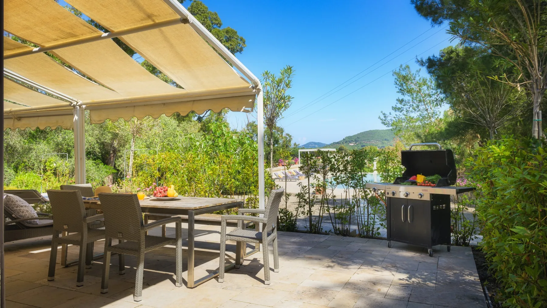 Una zona de comedor al aire libre bajo un toldo, con una parrilla cerca.