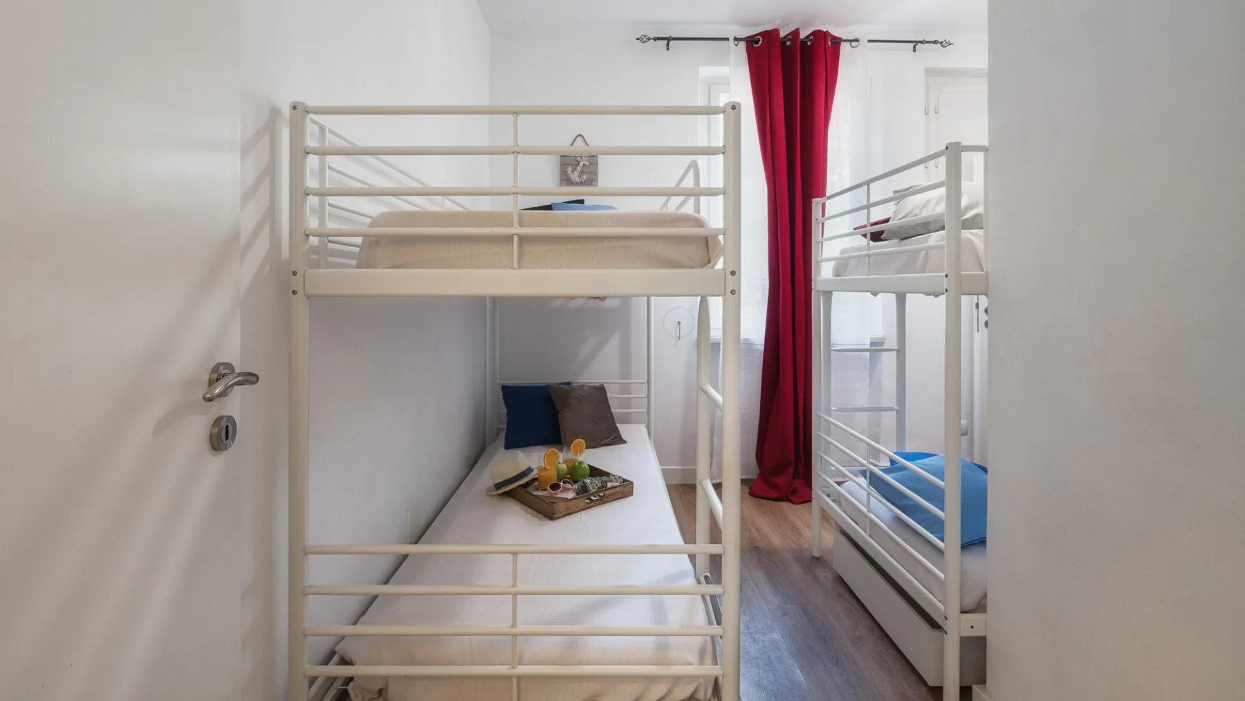 Una habitación luminosa con literas y una cortina roja junto a la ventana.