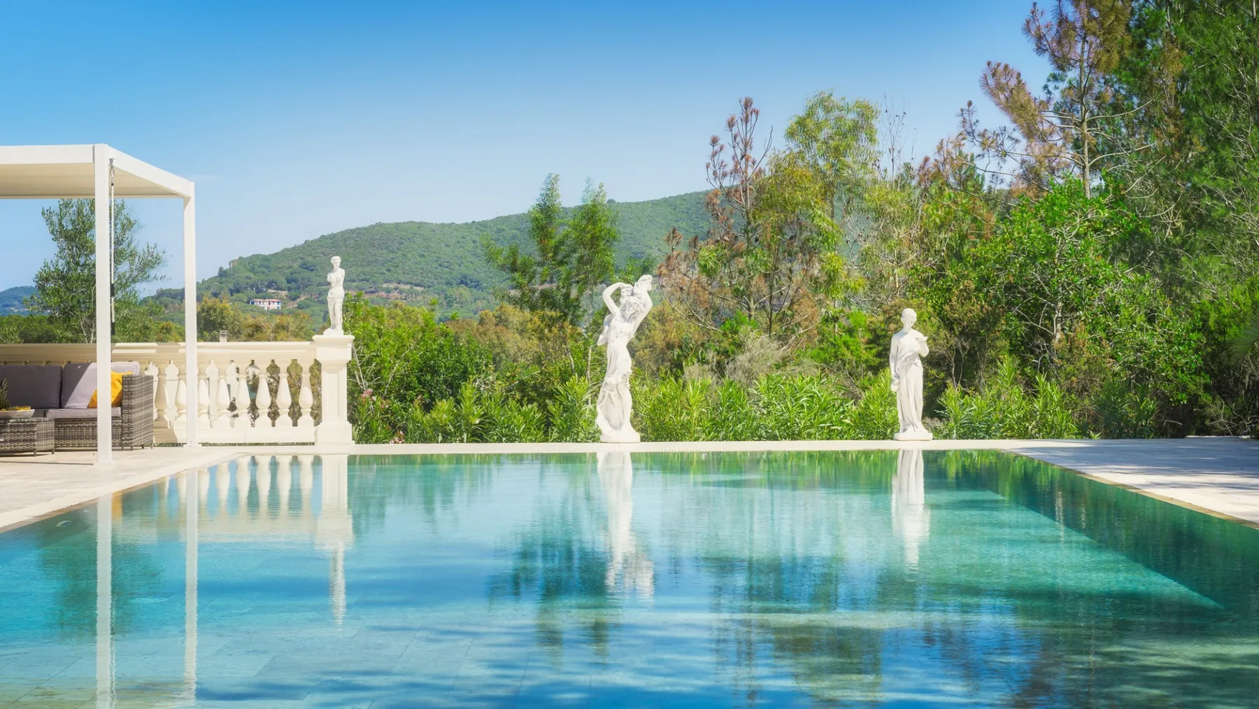 Una piscina al aire libre refleja los árboles y las estatuas cercanas.