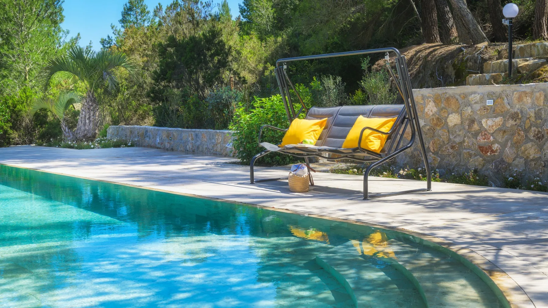 Una piscina al aire libre junto a una terraza pavimentada y un asiento colgante acolchado.