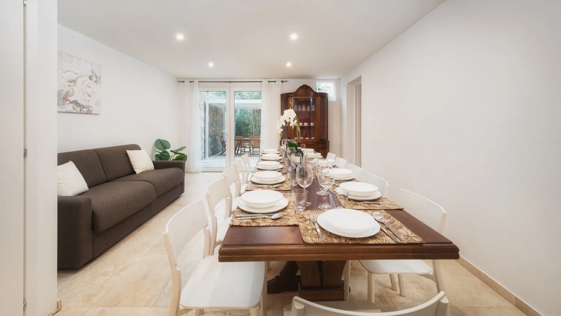 Comedor con una mesa puesta junto a un sofá y puertas de vidrio.
