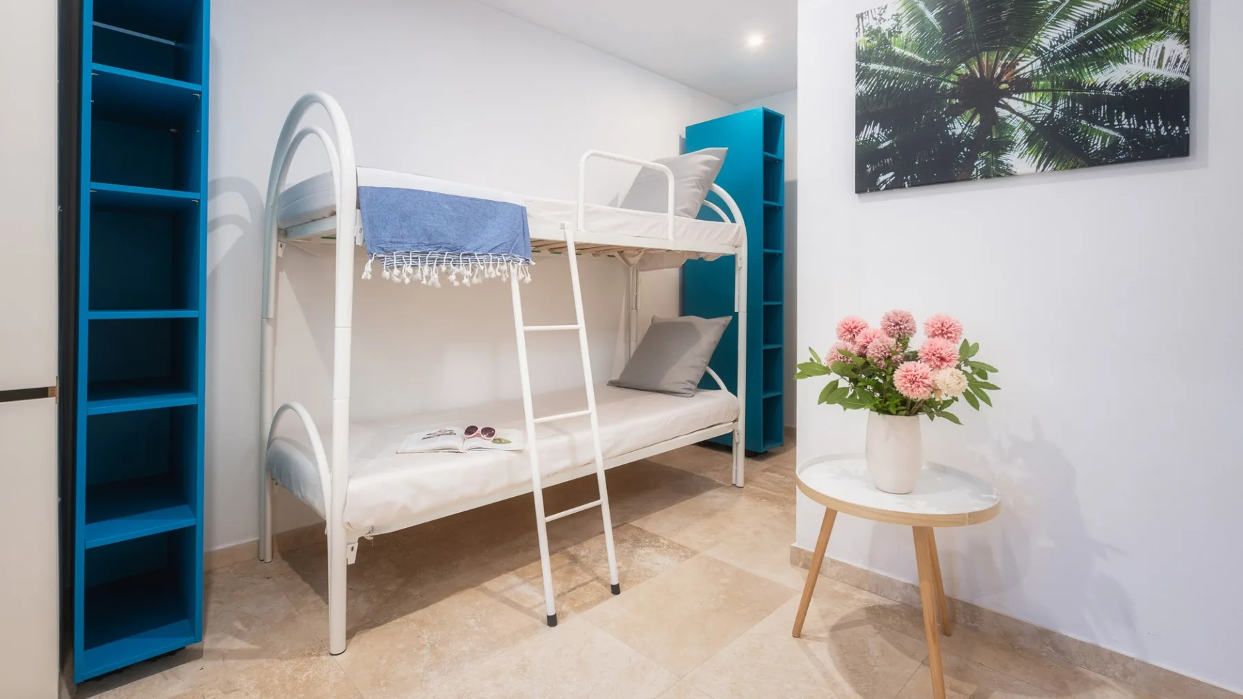 Un dormitorio luminoso con una litera blanca y una mesa pequeña con flores.