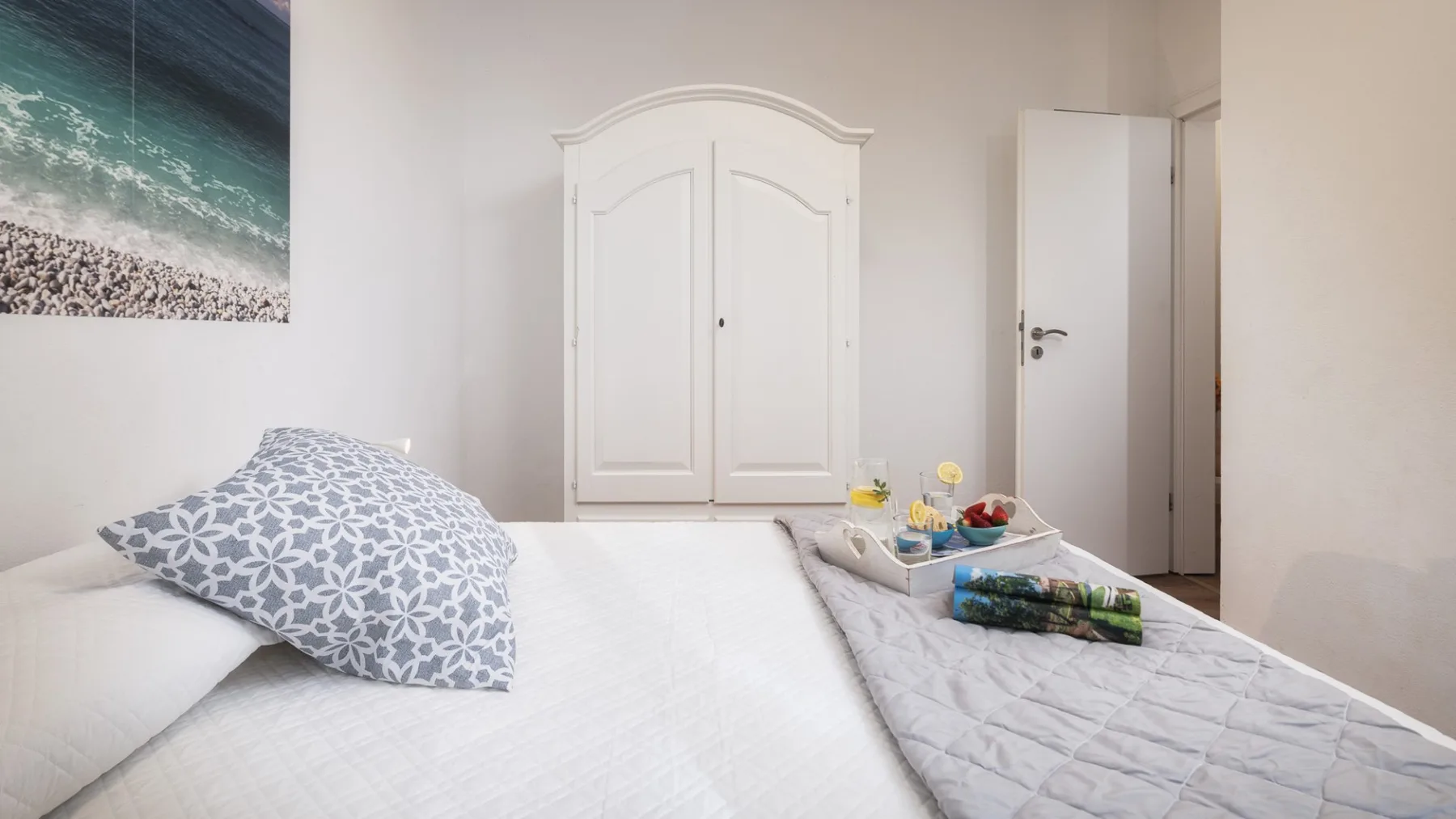 Un dormitorio luminoso con una cama, almohadas estampadas y un armario blanco.