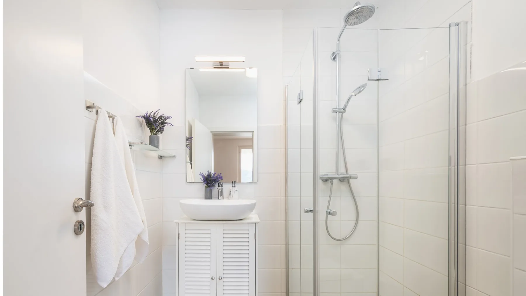 Un baño luminoso con lavabo, espejo y ducha de vidrio.