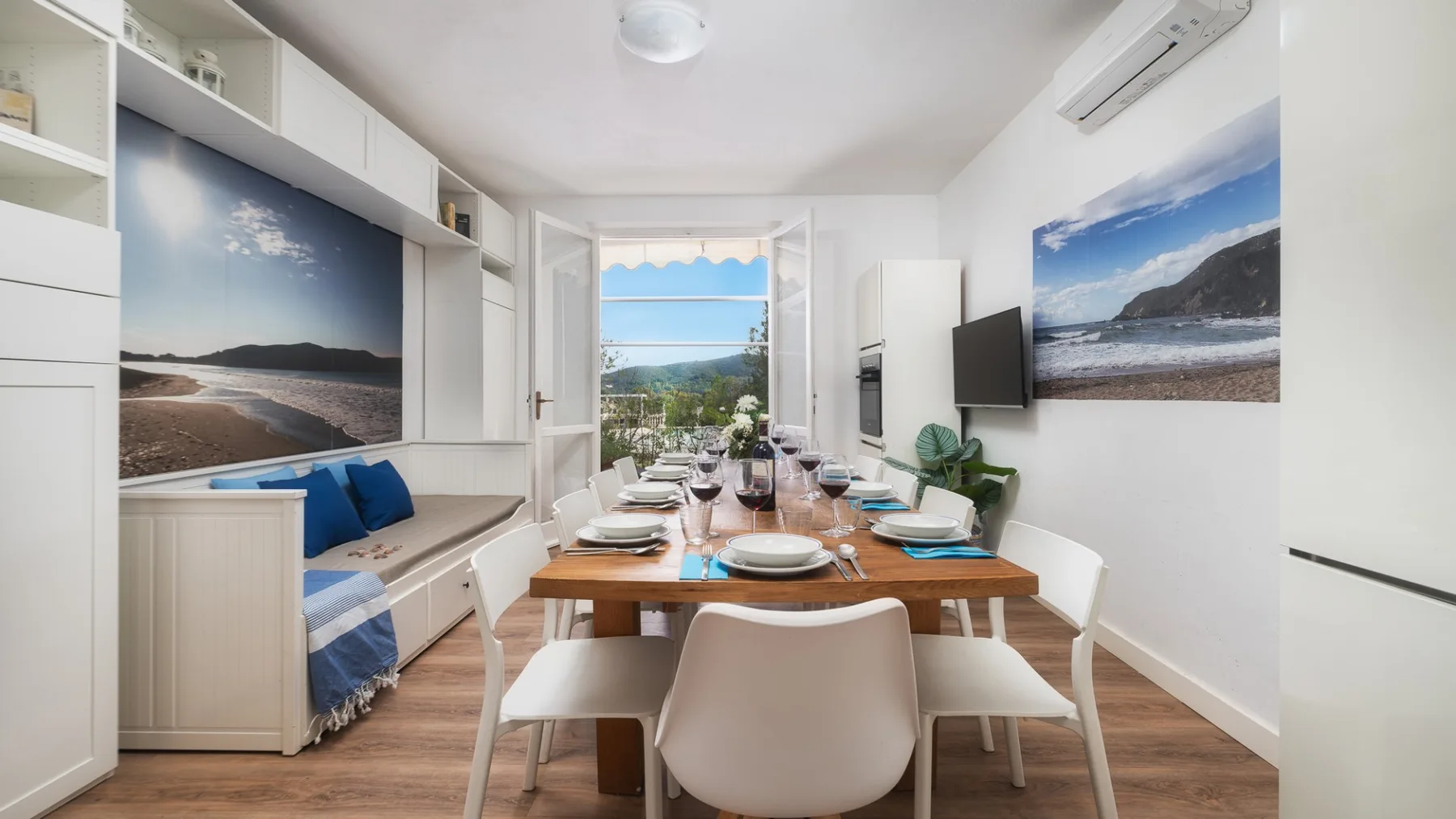 Un comedor luminoso con una mesa puesta y grandes fotografías costeras en las paredes.