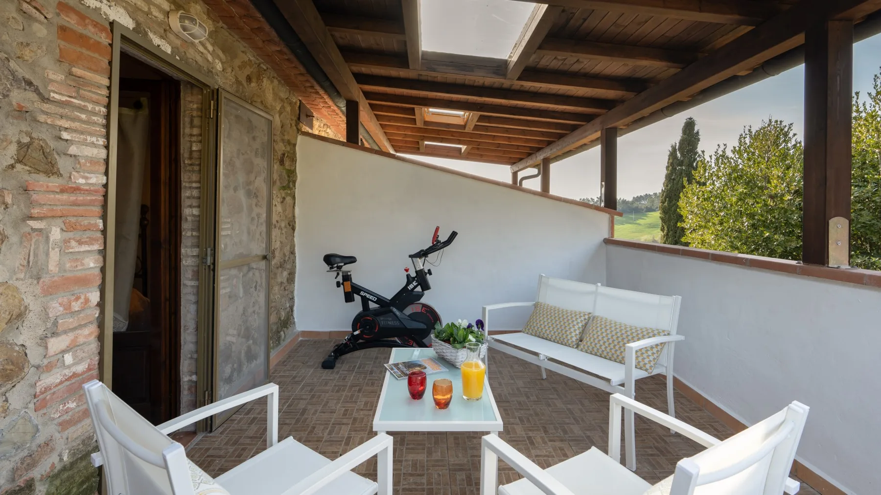 A covered outdoor seating area with a small table and exercise bike.
