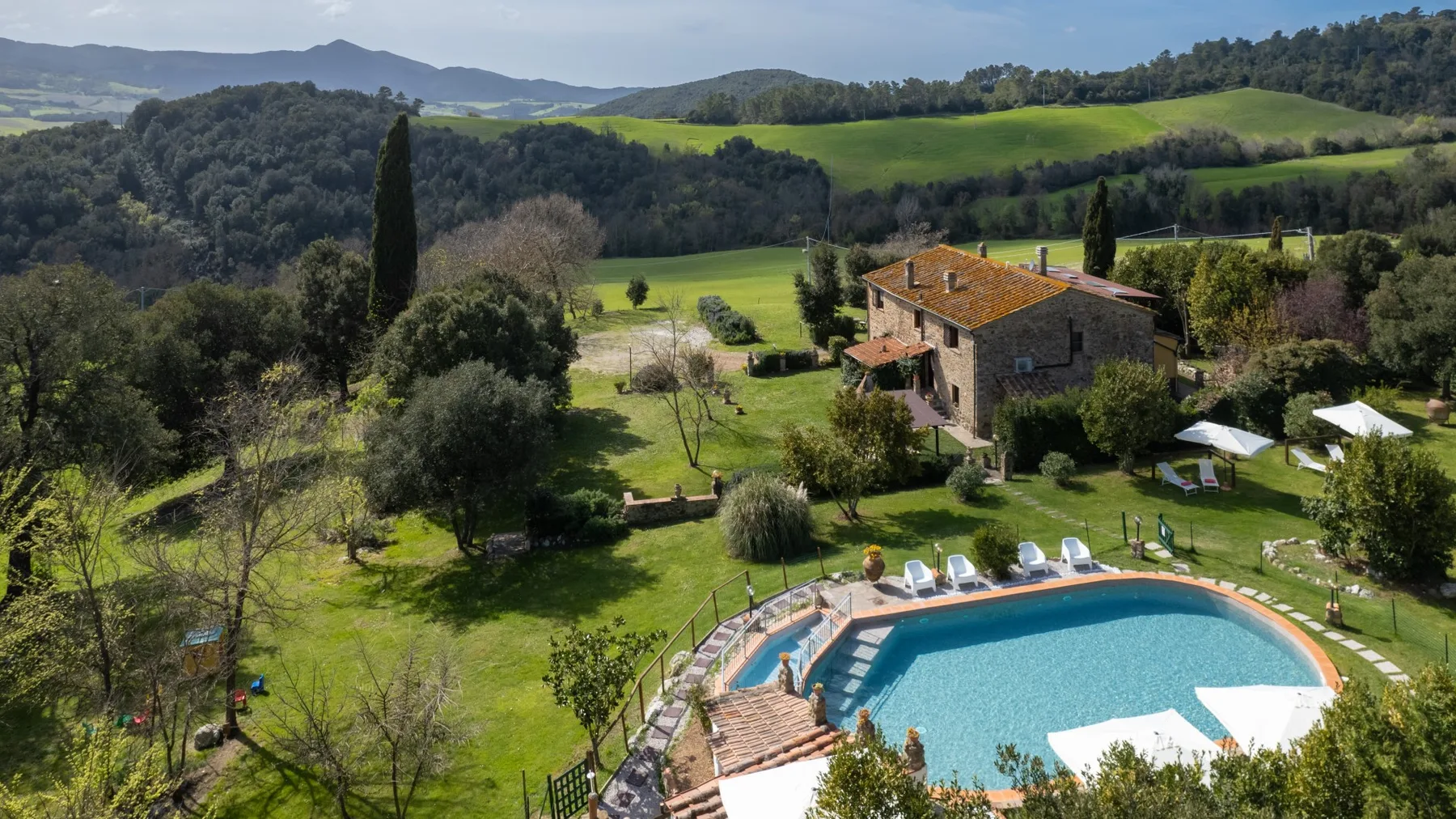 A countryside property with a curved swimming pool and green hills in the background.